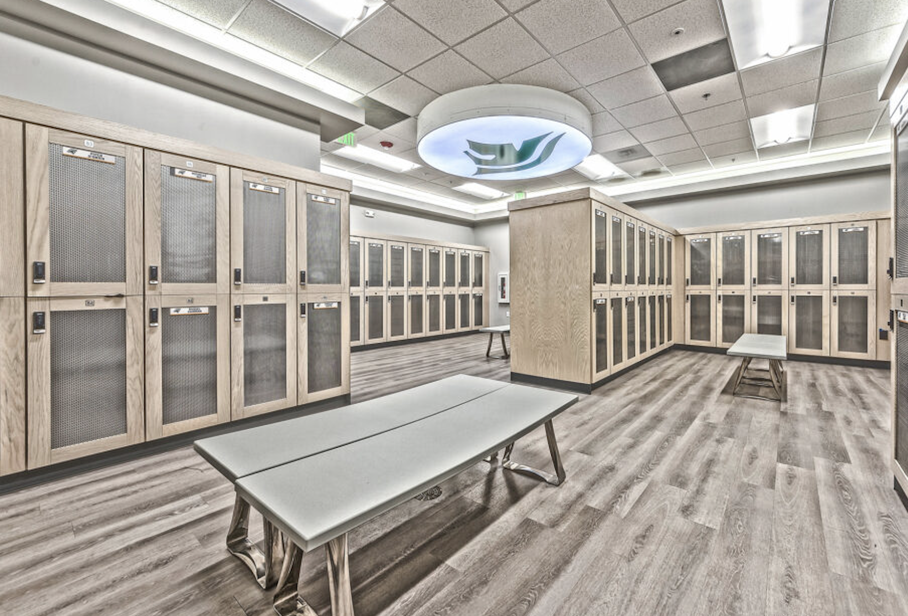 Empty changing room or locker room with wooden lockers, benches, and overhead lighting.
