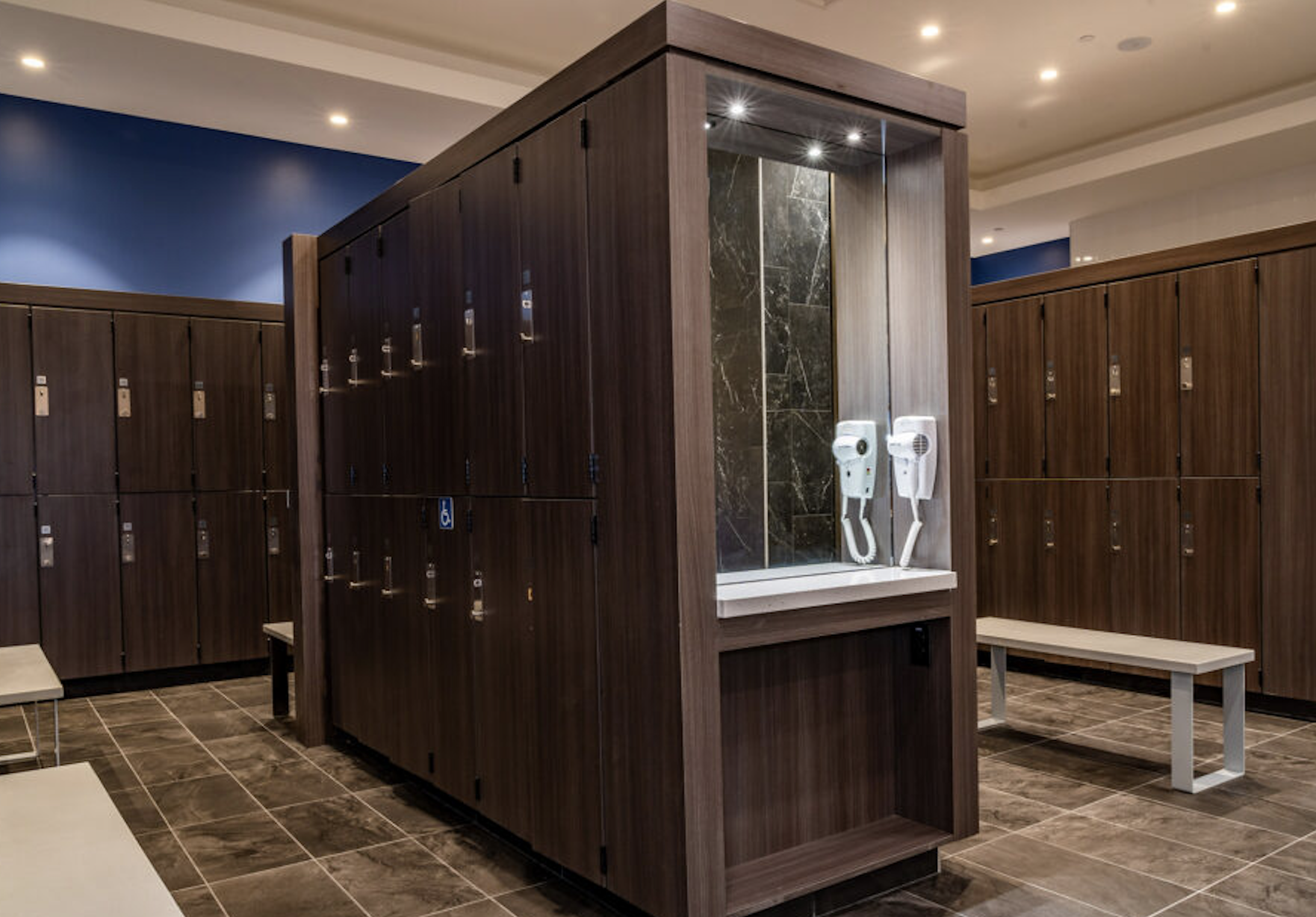 Locker room with wooden lockers, benches, and a shower station with wall-mounted hair dryers.