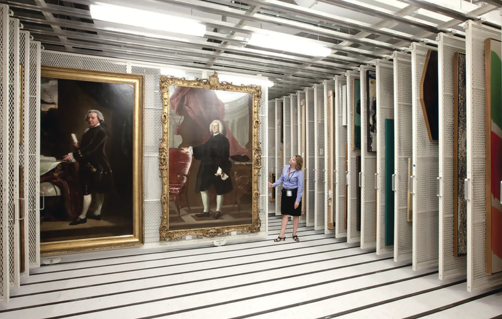 Museum storage area with two large portrait paintings and a woman observing them.