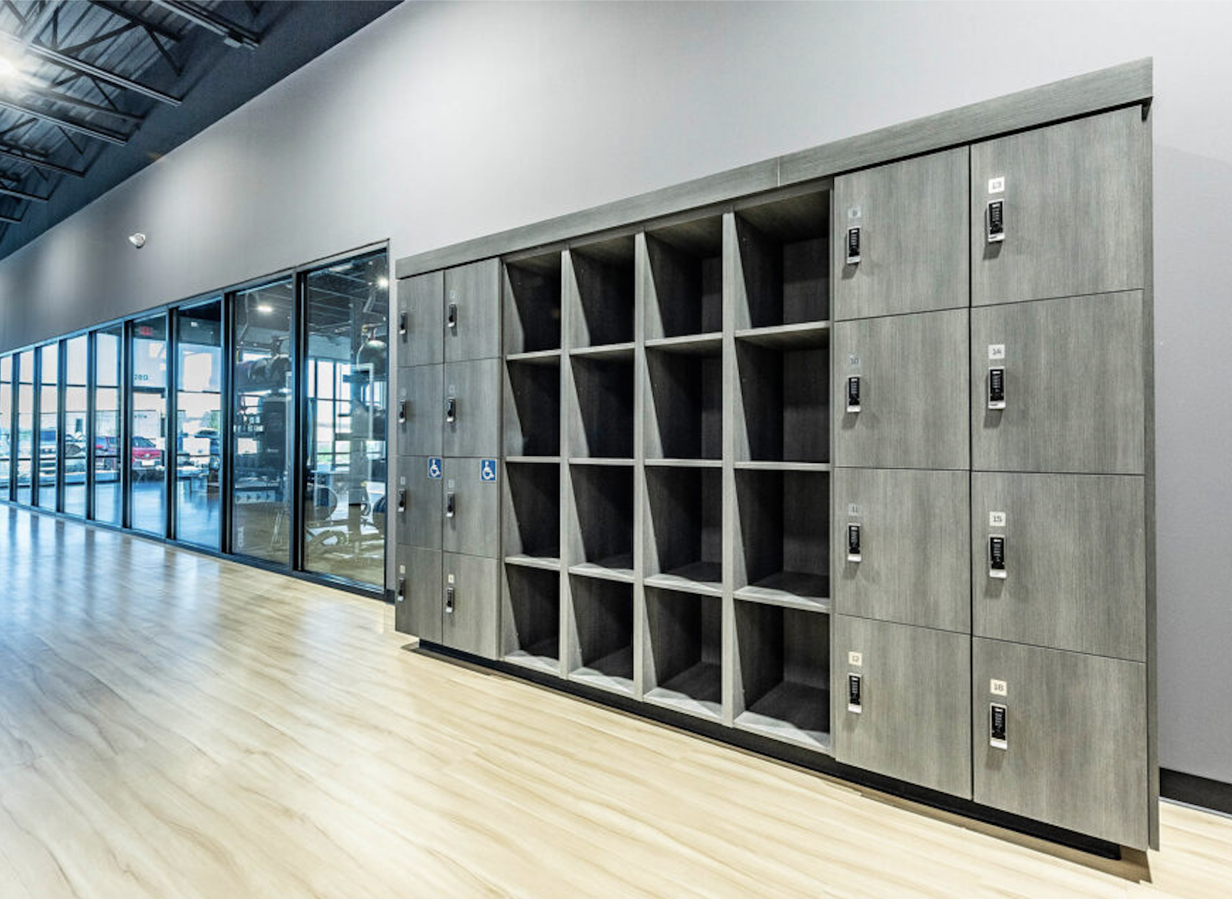 Row of wooden lockers and cubbies inside a modern gym or fitness center with glass walls and a wooden floor.