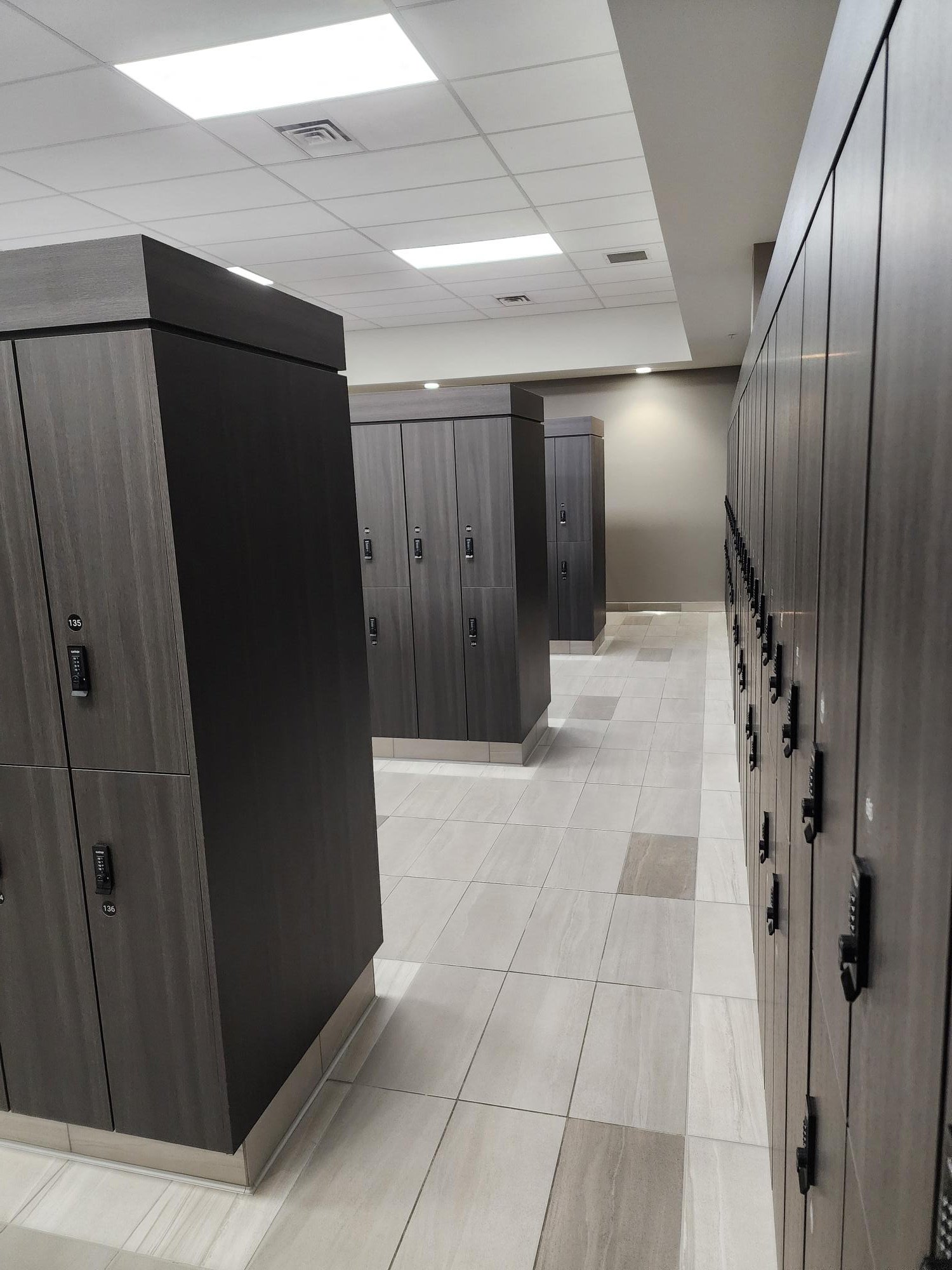 Empty locker room with grey and black lockers and tiled floor.