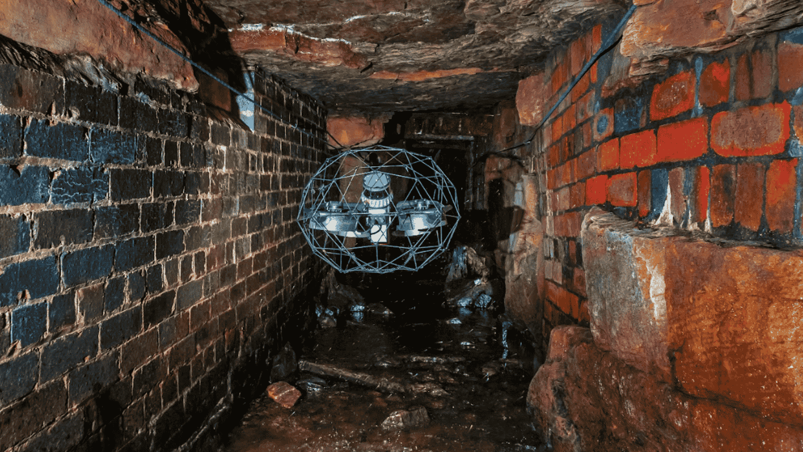 Flyability Elios 3 collision-tolerant drone inspecting a confined space brick tunnel.
