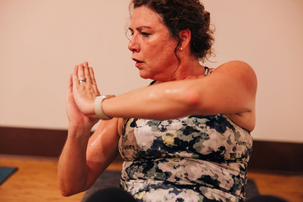 Woman practicing yoga in a seated position with hands pressed together in prayer pose, wearing a camouflage-patterned tank top.