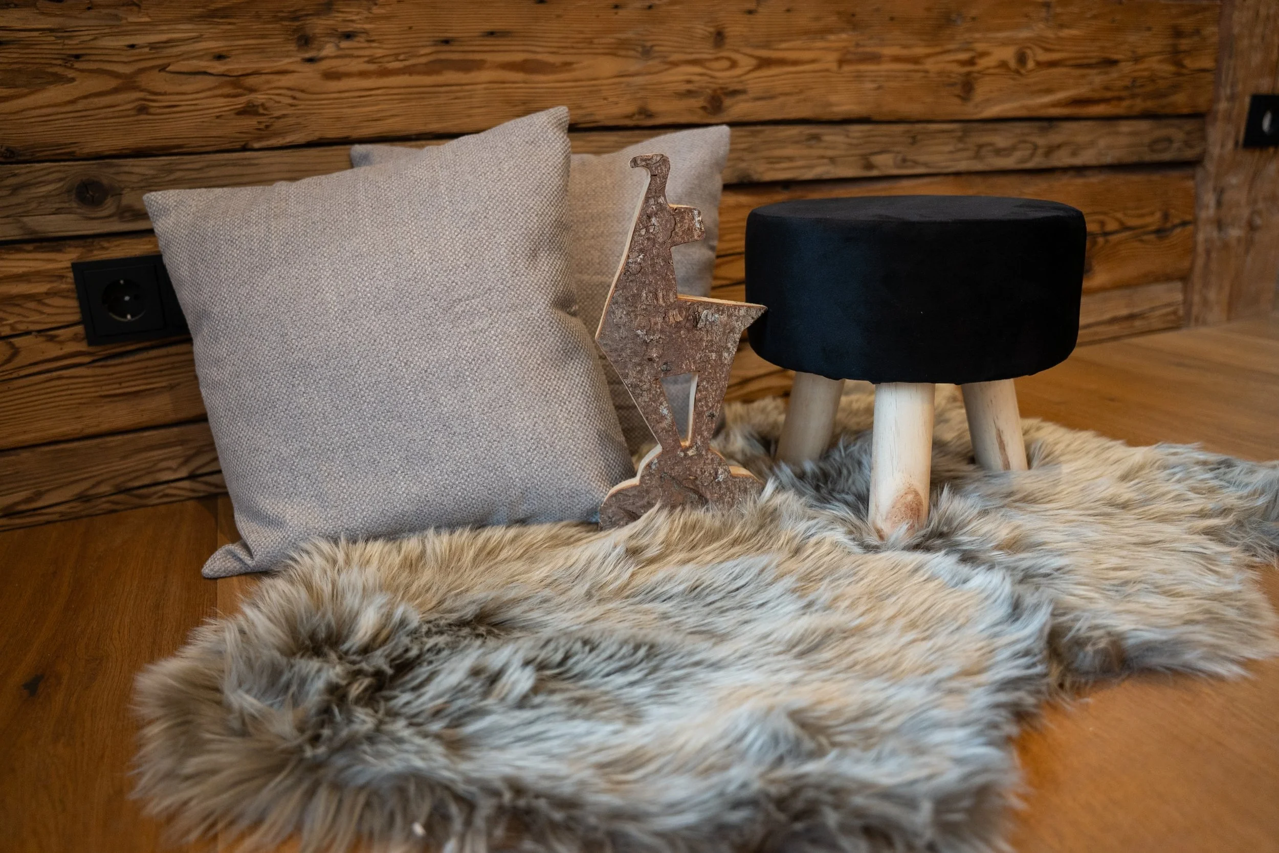 Kaminumgebung mit Kissen, einem rustikalen Metallreittier, kleines schwarzes Hocker und Fellteppich auf Holzdielen