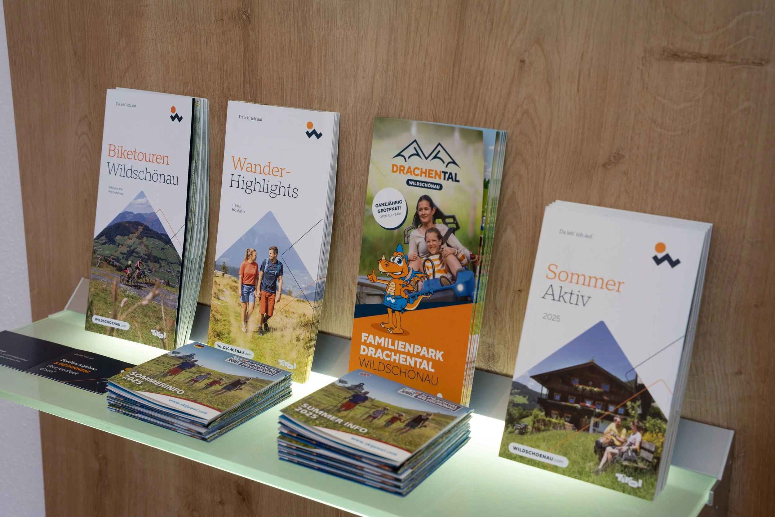 Informationsmaterial über Outdoor-Aktivitäten, darunter Mountainbike-Touren, Wandern Highlights und Familienpark Drachental, auf einem Tisch ausgestellt.