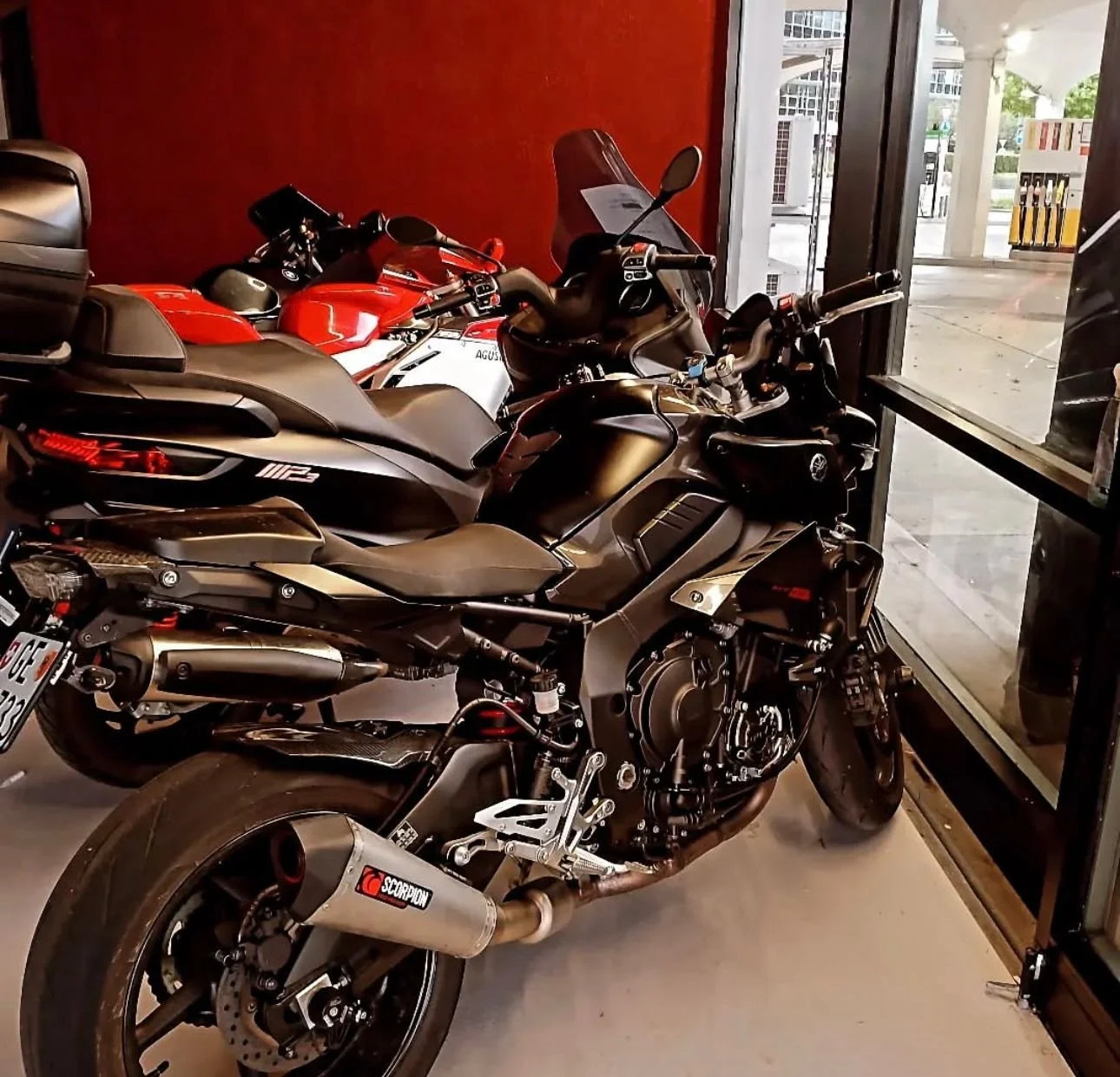 Deux motos garées dans un intérieur, l'une noire et l'autre rouge.