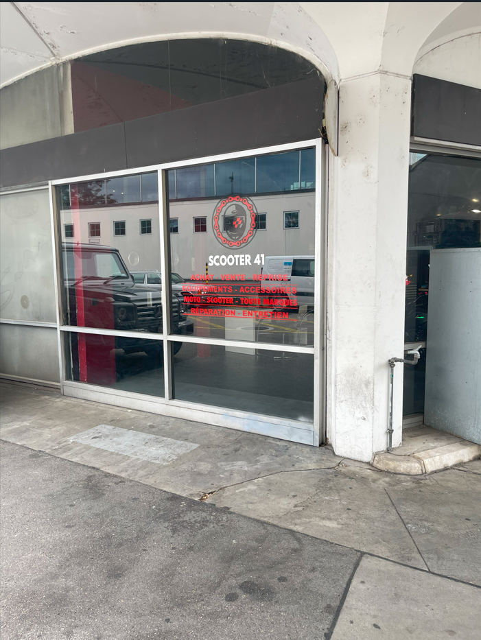 Vitrine d'un magasin de scooters avec marquages rouges indiquant "Scooter 41, achat, vente, reprise, équipements, accessoires, moto, scooter, toutes marques, réparation, entretien".