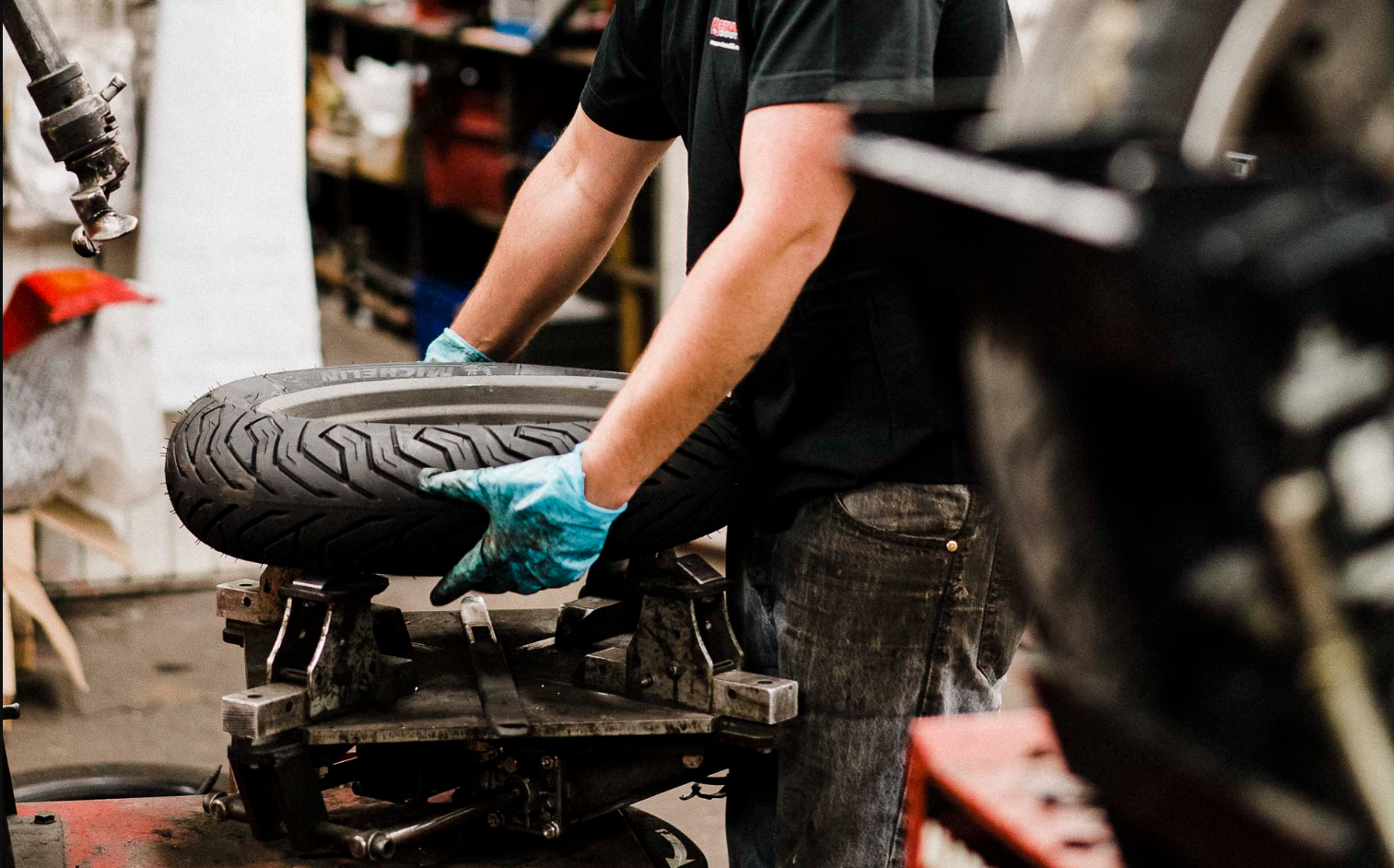 Un mécanicien en train de manipuler un pneu avec des gants, dans un atelier de réparation automobile.