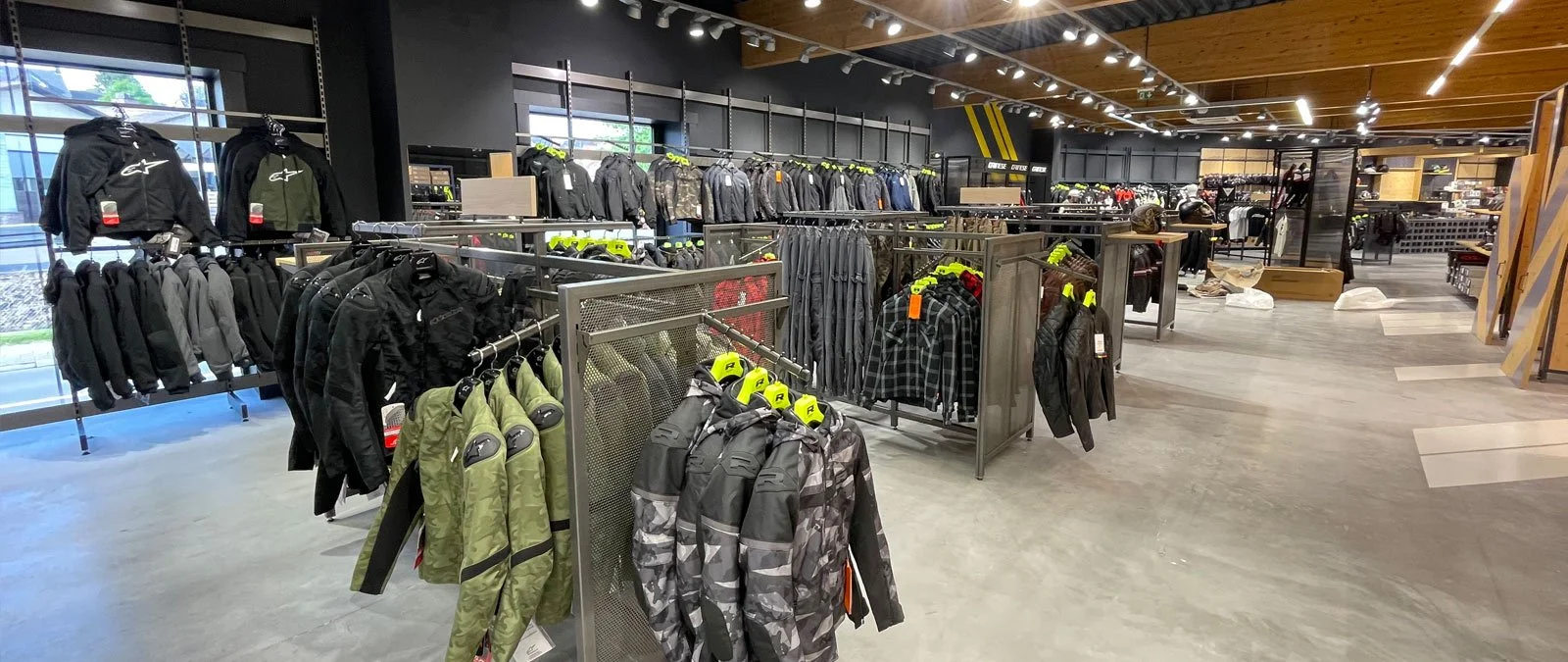 Intérieur d'un magasin de vêtements de moto avec divers blousons exposés sur des présentoirs métalliques.