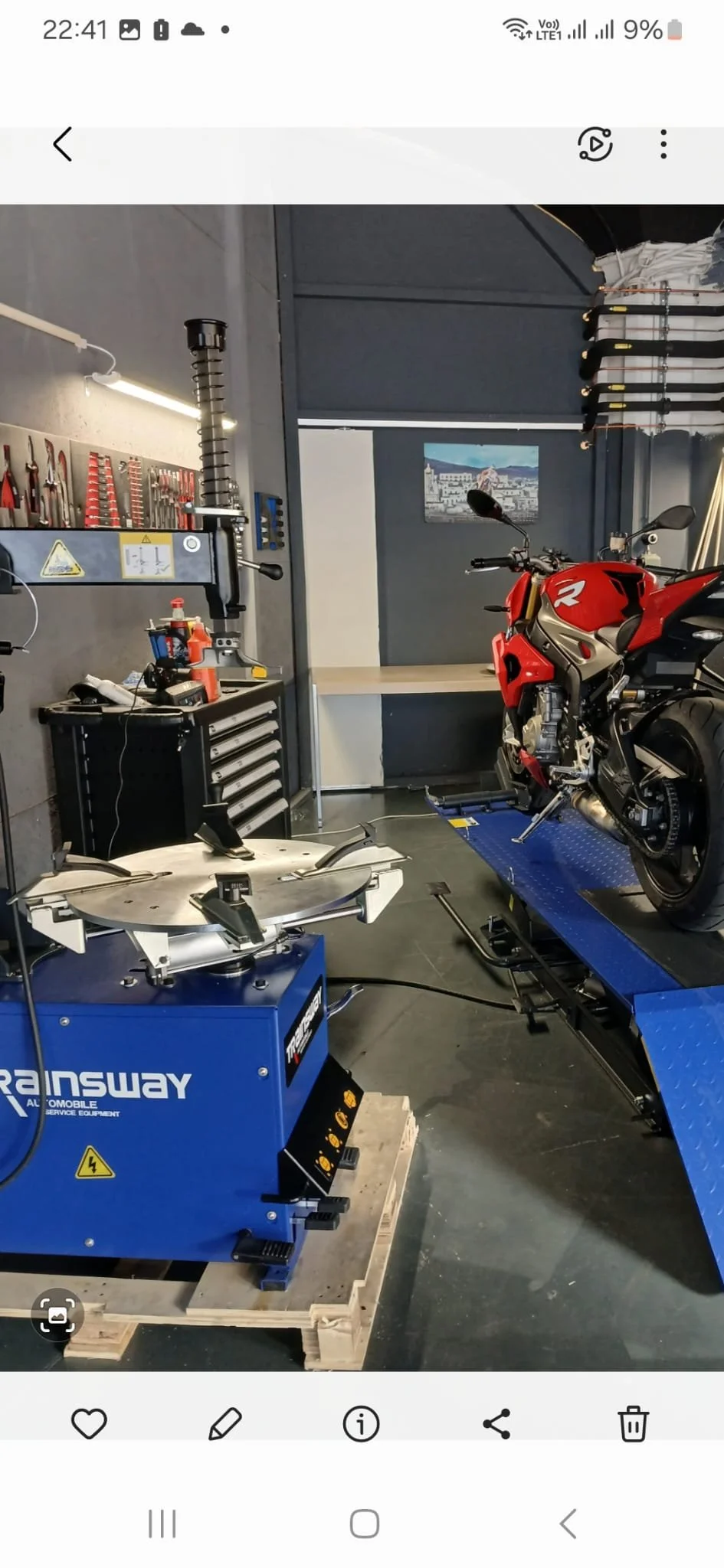 Garage avec moto rouge, machine de service automobile et outils au mur.