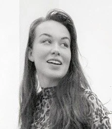 Ung kvinna med långt, mörkt hår, ler och tittar åt sidan, i svartvitt.