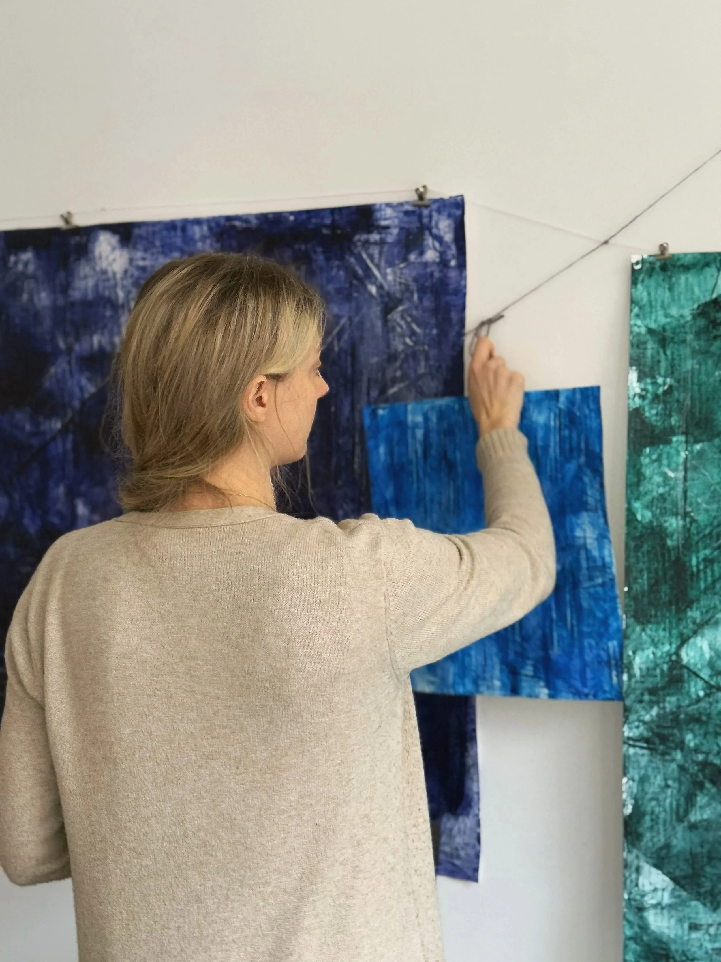 En kvinna som hänger upp konstverk på en vit vägg.