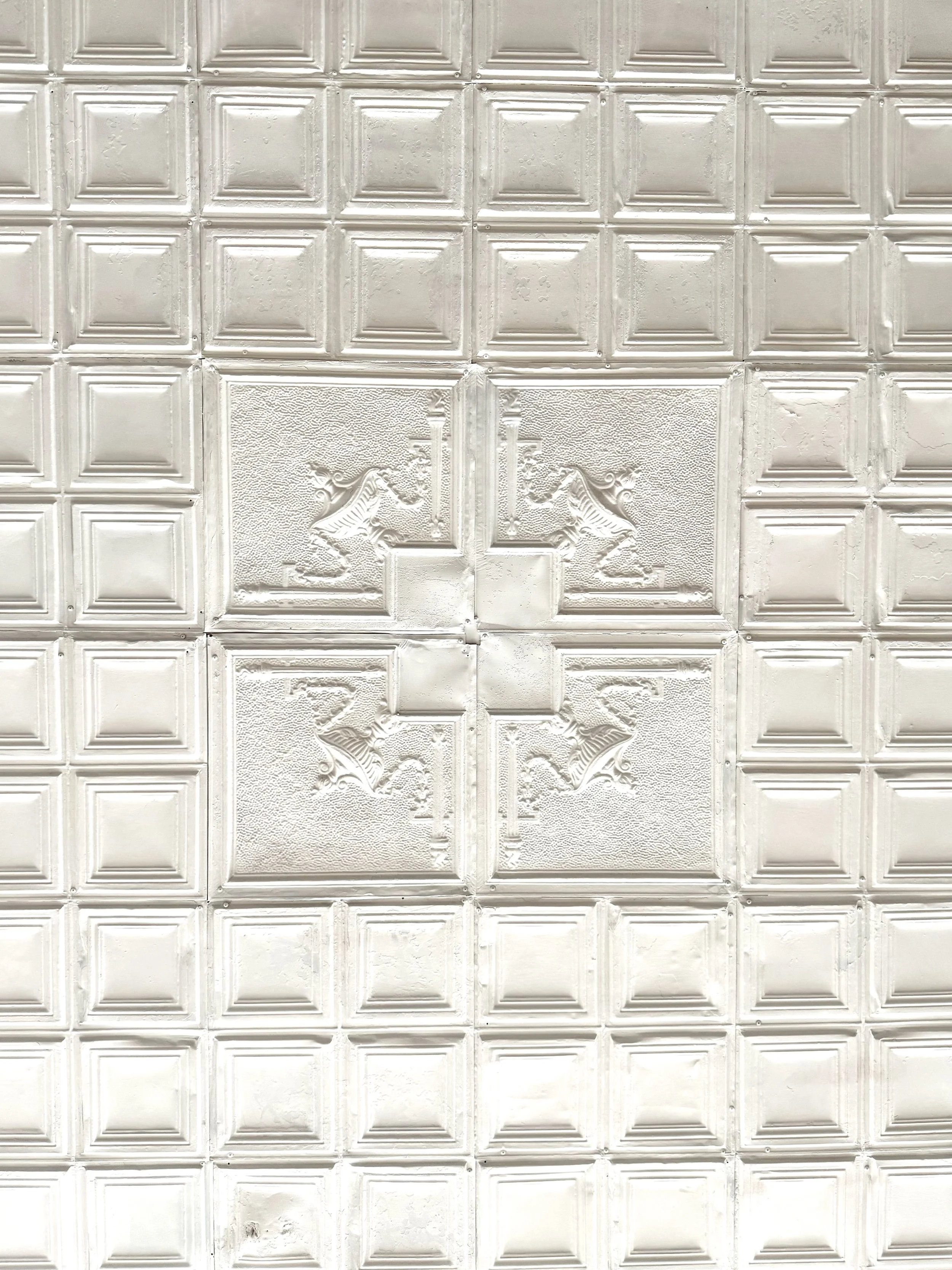 Close-up of decorative white ceiling tiles with embossed patterns, including lion figures and geometric designs.