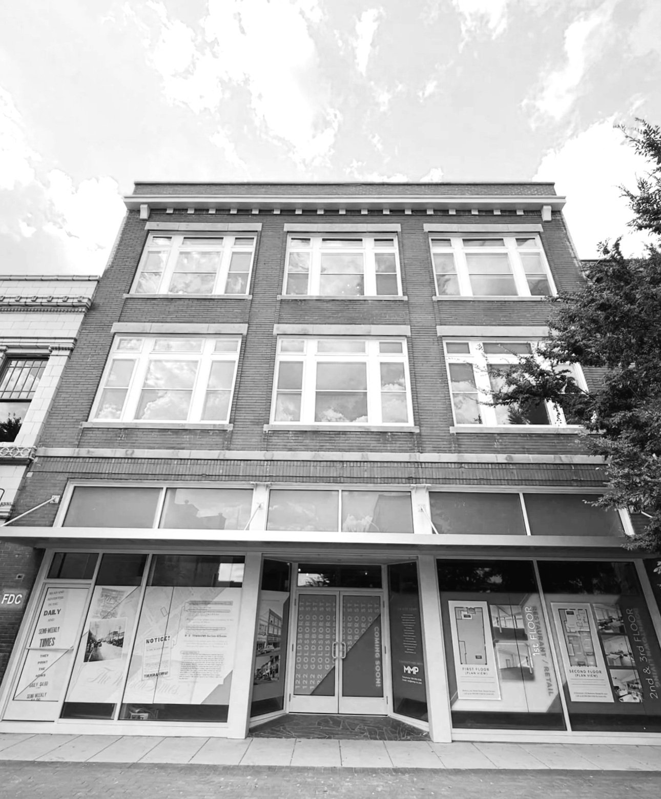 Black and white photo of a multi-story brick building with large windows and commercial space on the ground floor.