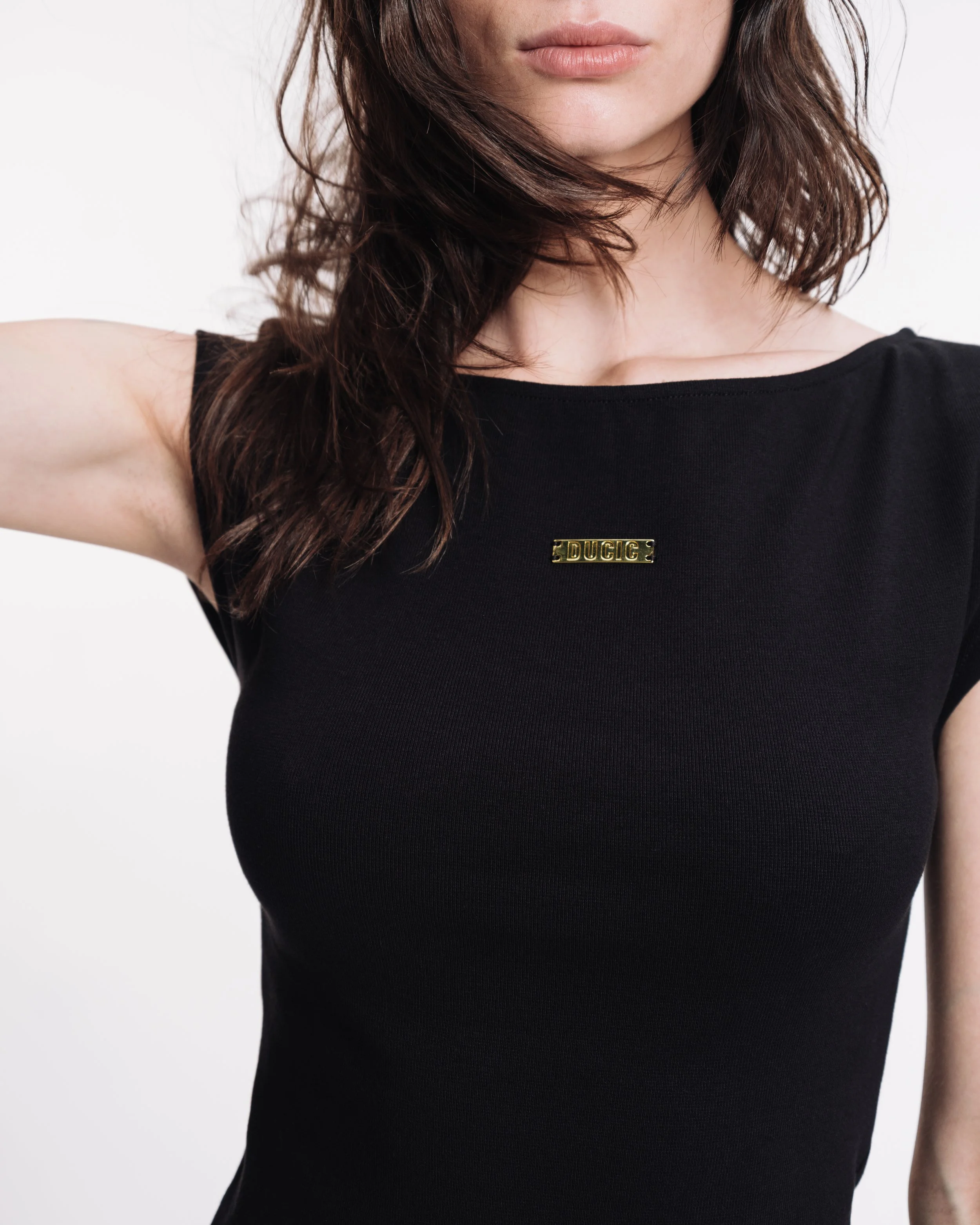 Close-up of a woman wearing a black top with a small gold nameplate that says 'DUCIC' on the chest.