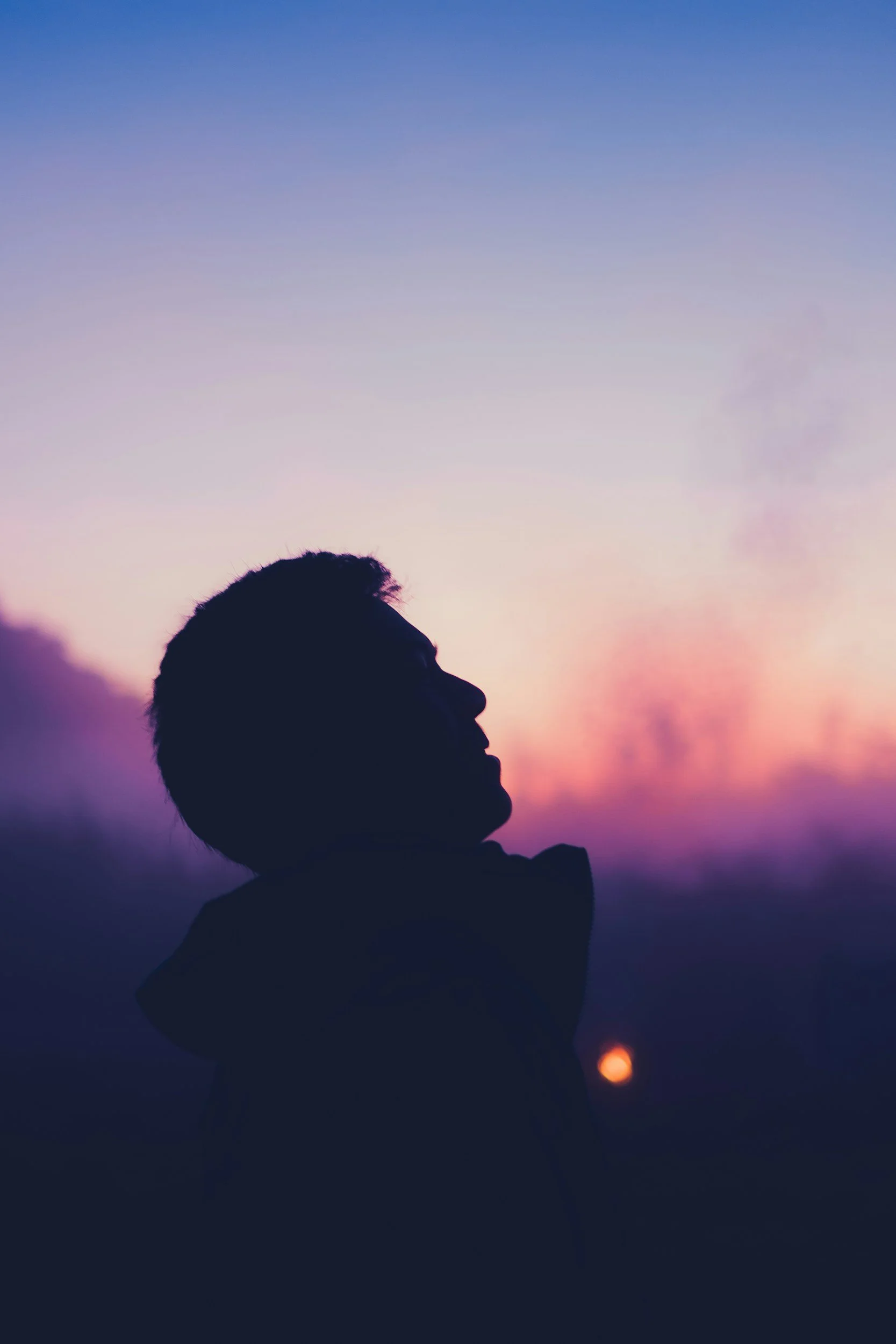 Silhouette of a person in profile against a colorful pink and purple sunset sky
