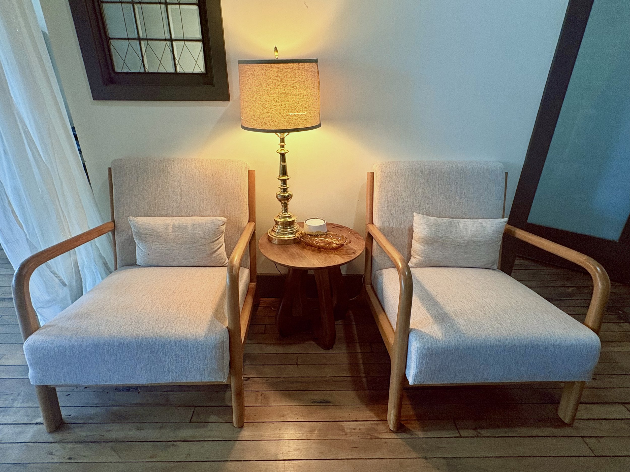 Two upholstered armchairs flank a small wooden table with a lit lamp in a cozy sitting area.