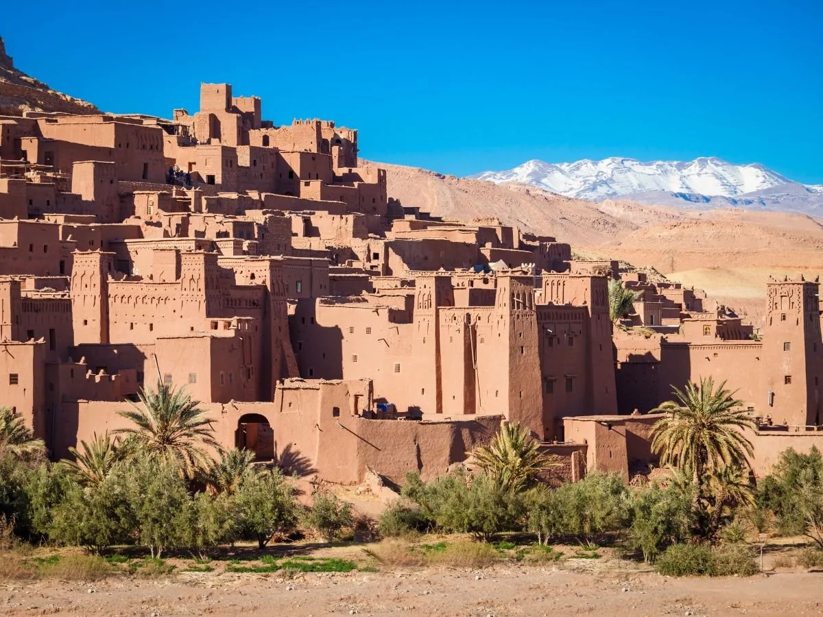 Panorama dello storico ksar fortificato di Ait-Ben-Haddou in terra battuta con le montagne innevate dell'Atlante sullo sfondo in Marocco.