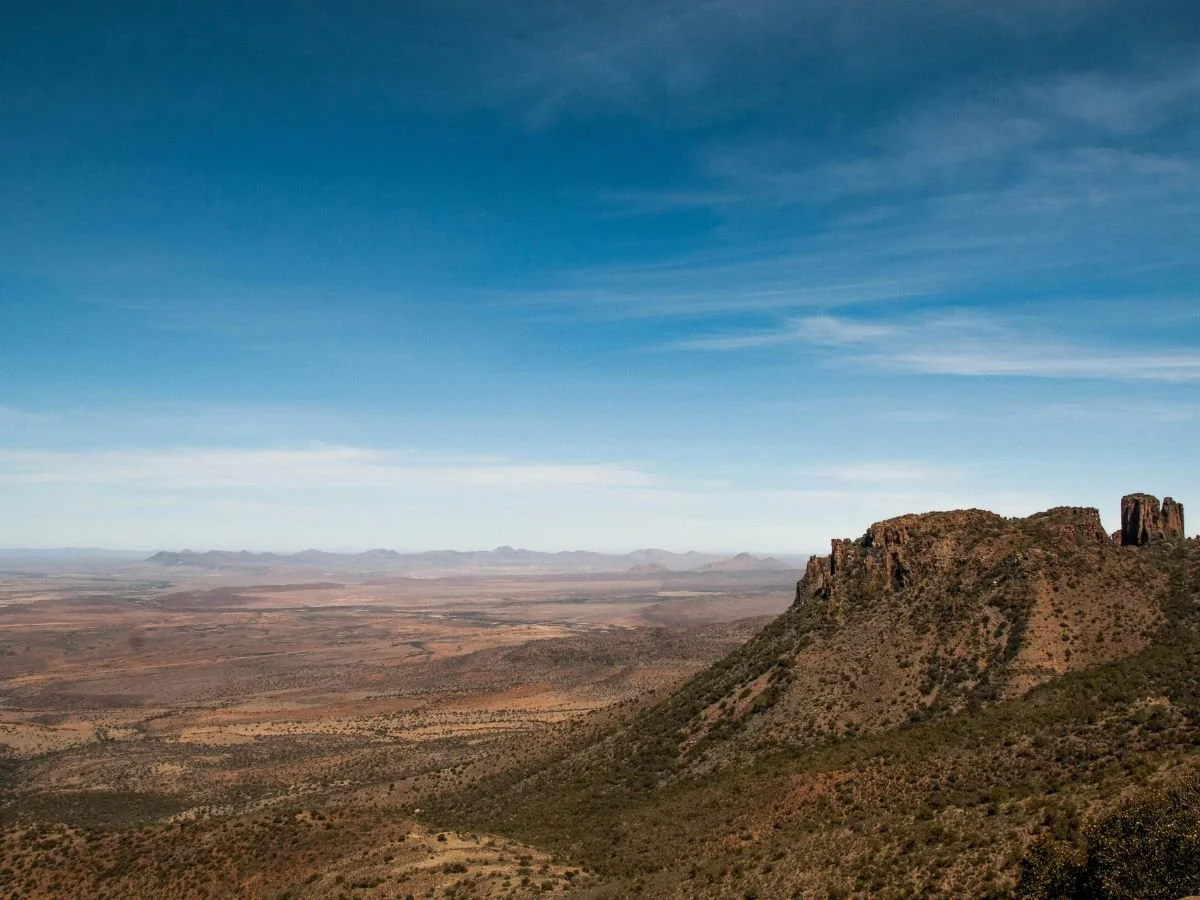 Paesaggio semidesertico del Karoo con altopiano roccioso e vasta pianura sotto un cielo azzurro