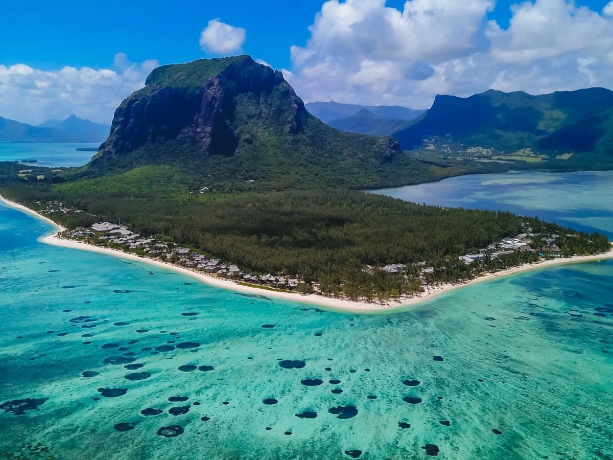 Vista aerea di un'isola tropicale con un'imponente montagna verde circondata da una lussureggiante foresta. Le acque turchesi dell'oceano e le spiagge di sabbia bianca aggiungono un tocco di serenità.