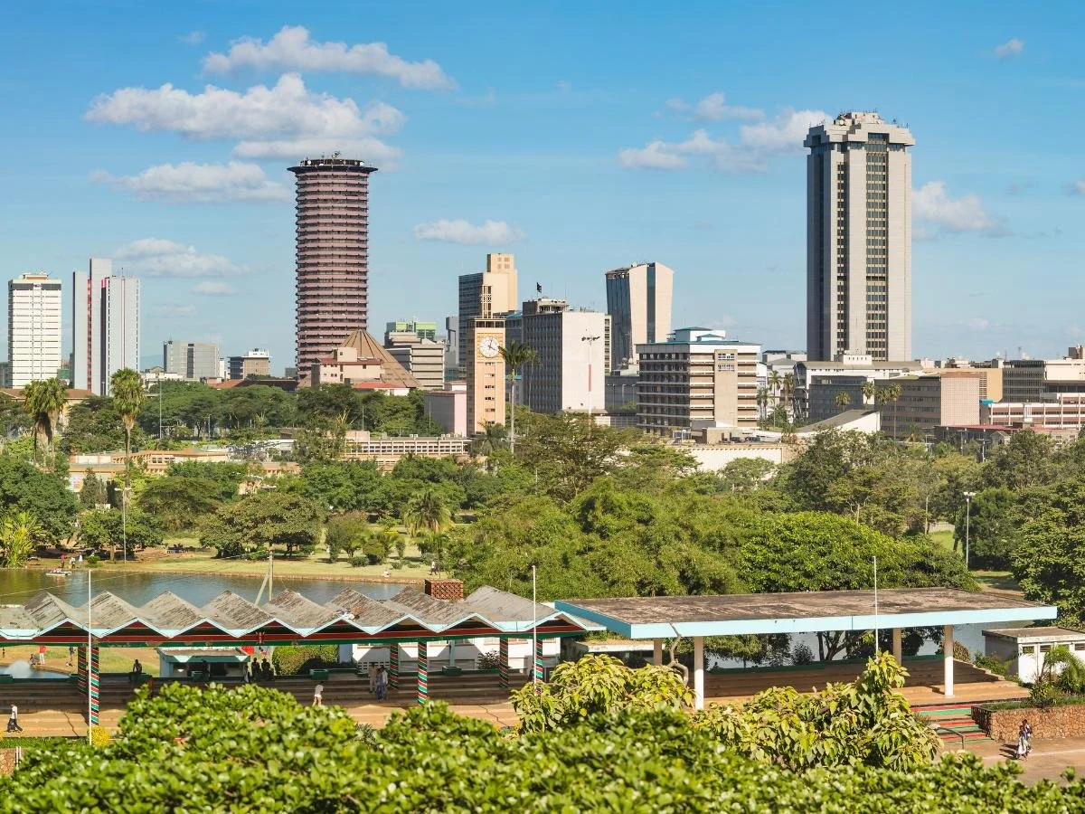 Lo skyline di Nairobi, in Kenya, con i suoi moderni grattacieli, tra cui una torre cilindrica, incorniciati da una vegetazione lussureggiante sotto un cielo azzurro brillante con soffici nuvole.