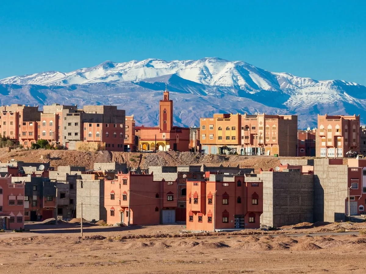 Architettura tradizionale di Ouarzazate con palazzi in adobe rosso e cime innevate sullo sfondo.