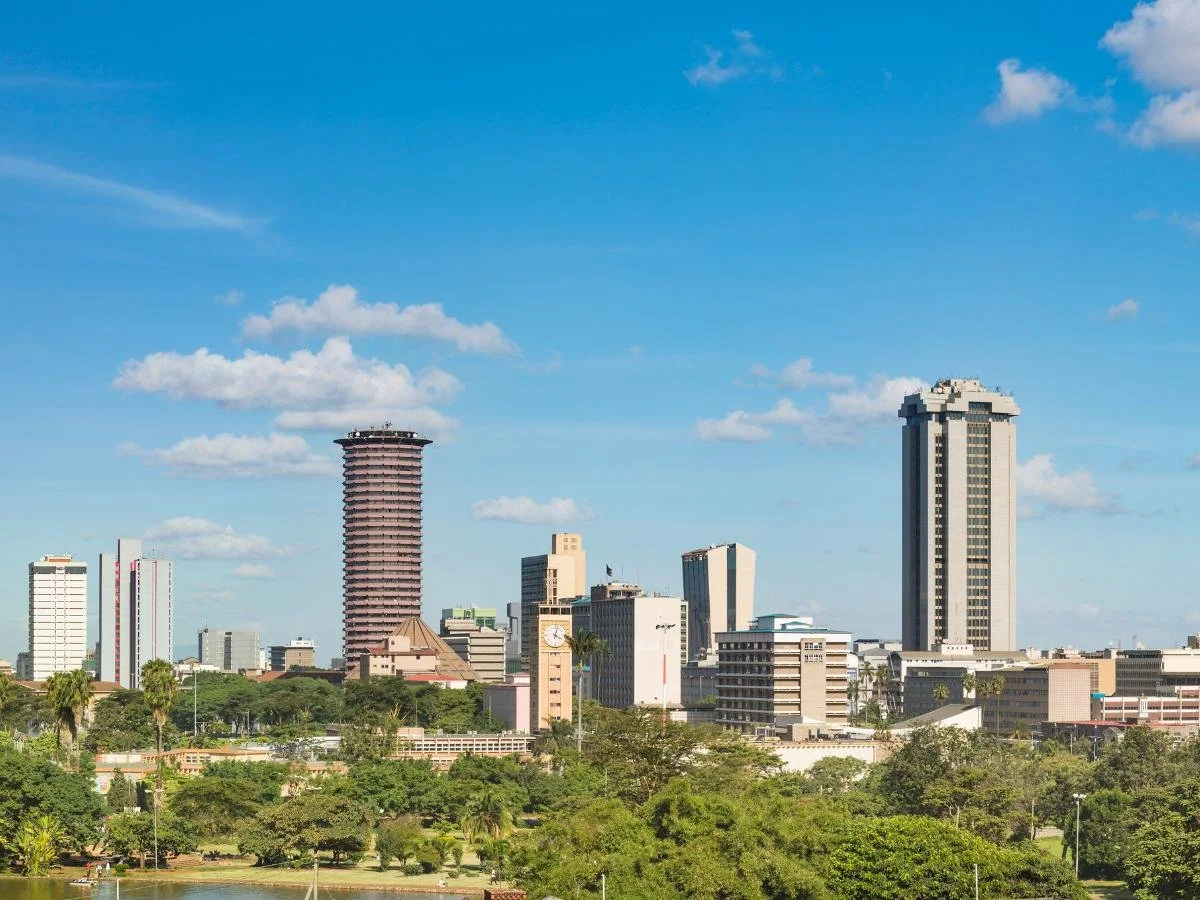 Lo skyline di Nairobi, in Kenya, con moderni grattacieli e una vegetazione lussureggiante sotto un cielo azzurro brillante con nuvole sparse, trasmettendo vivacità urbana.