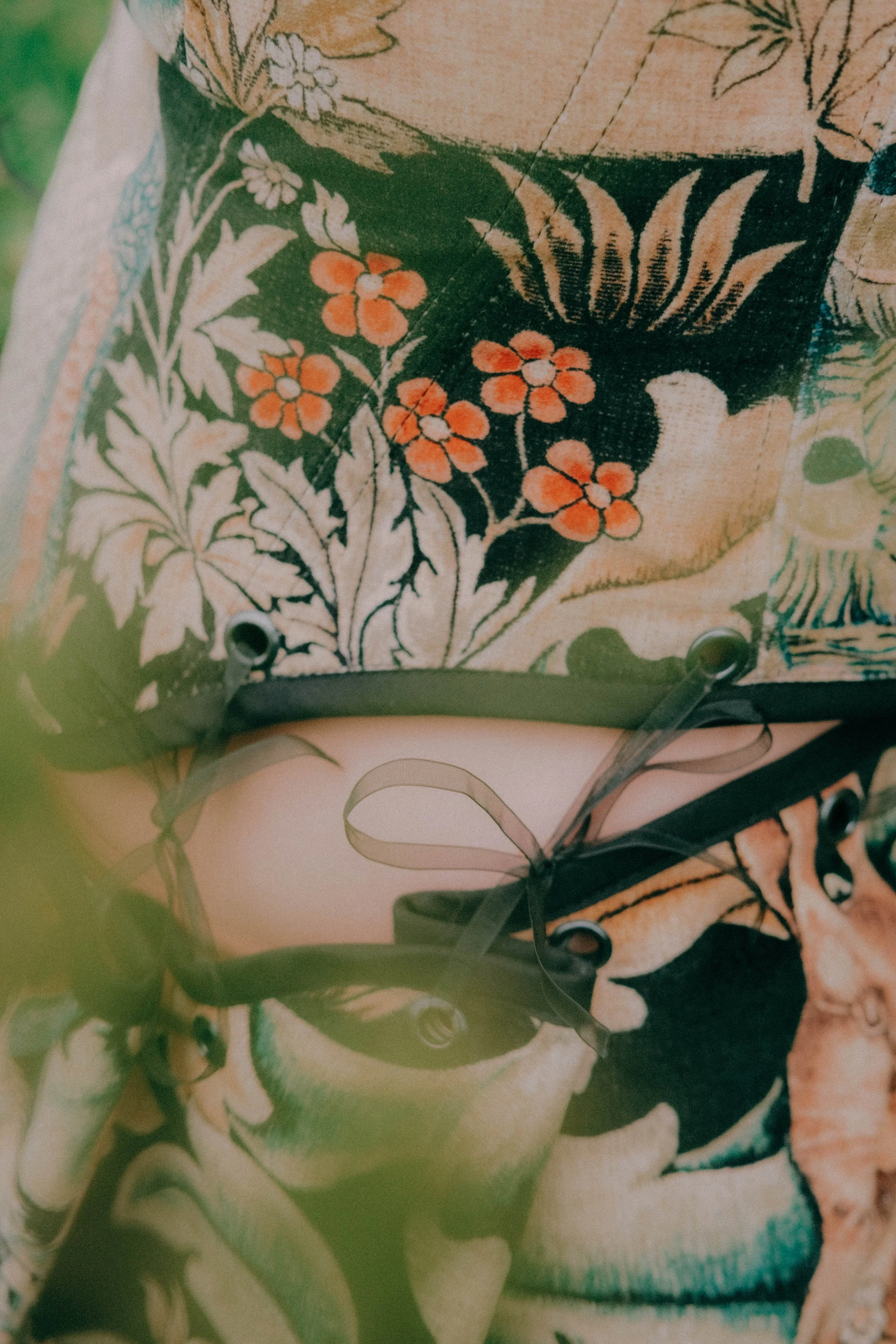 Close-up of a floral-patterned garment with orange flowers and green leaves, tied at the waist with a black ribbon.