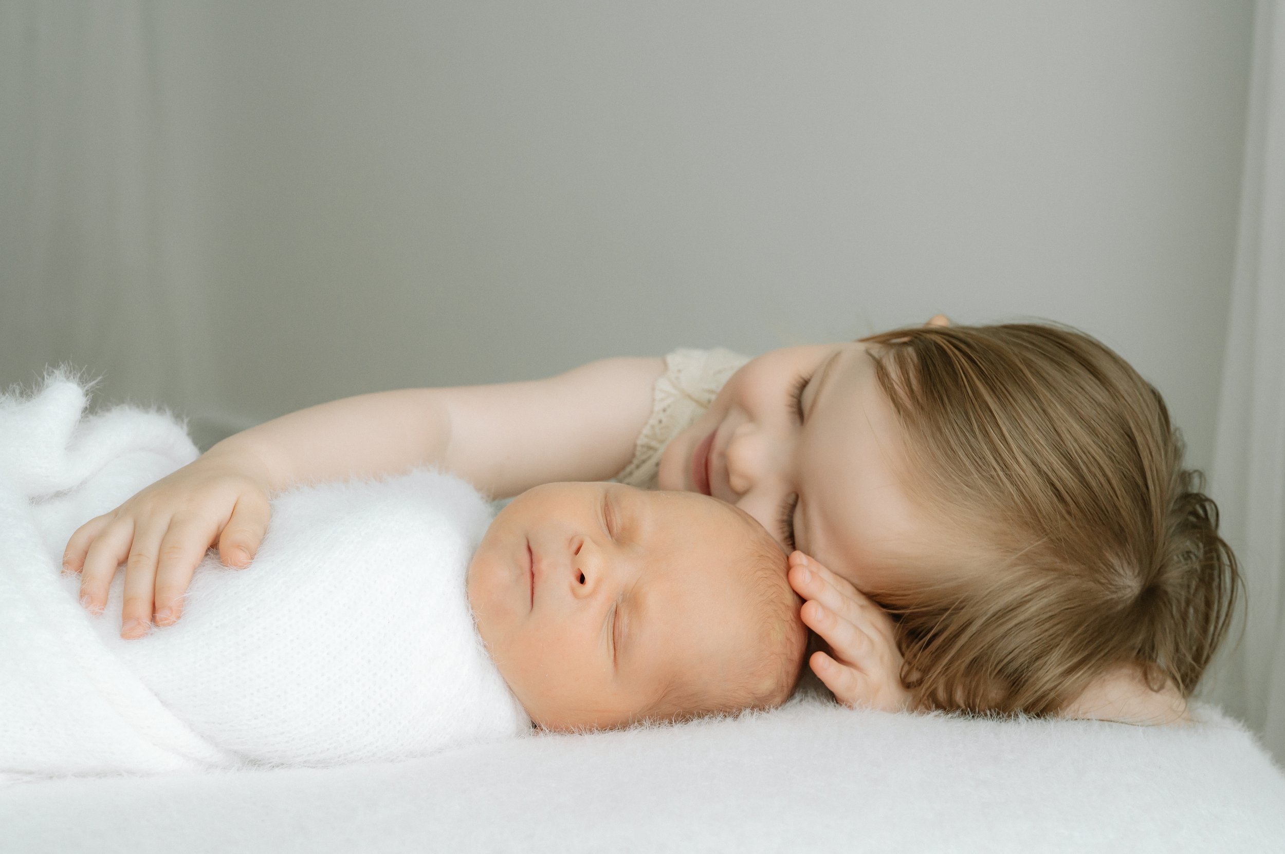 toddler cuddling newborn sibling in neutral studio