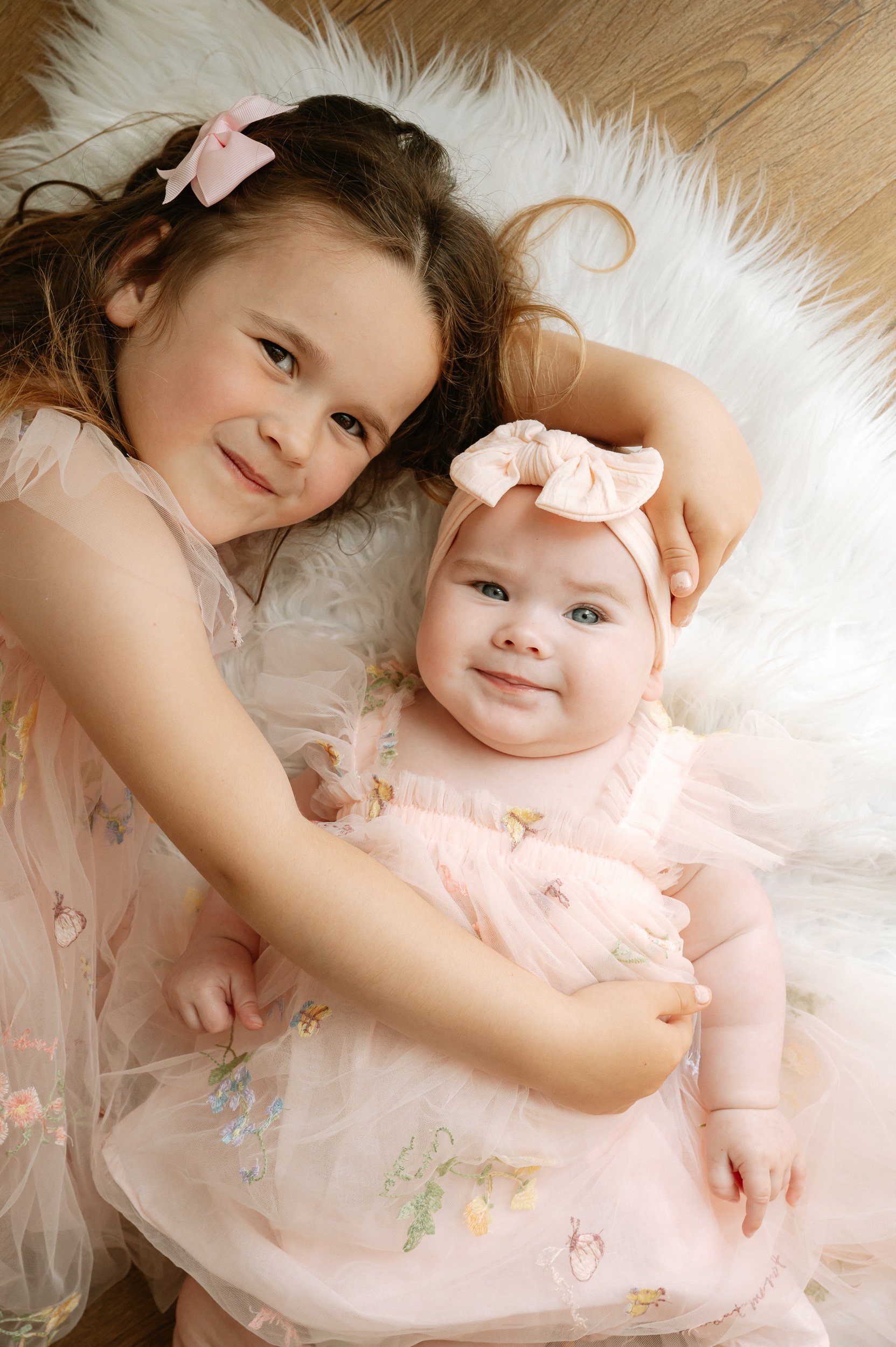 Portrait of a smiling older sister cuddling her baby sibling during a natural light family photography session in Doncaster.