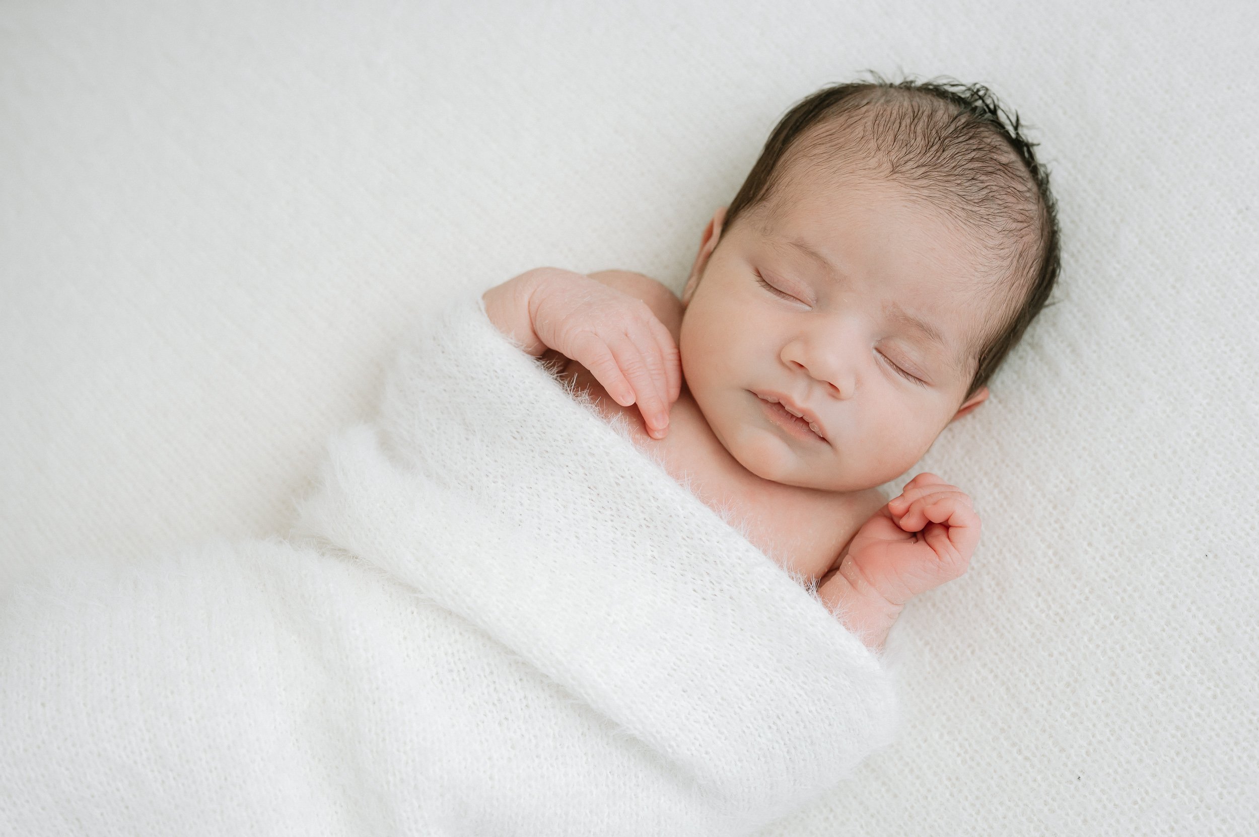 Portrait of a peacefully sleeping newborn baby wrapped in a soft white blanket, captured in a natural light photography studio in Doncaster.
