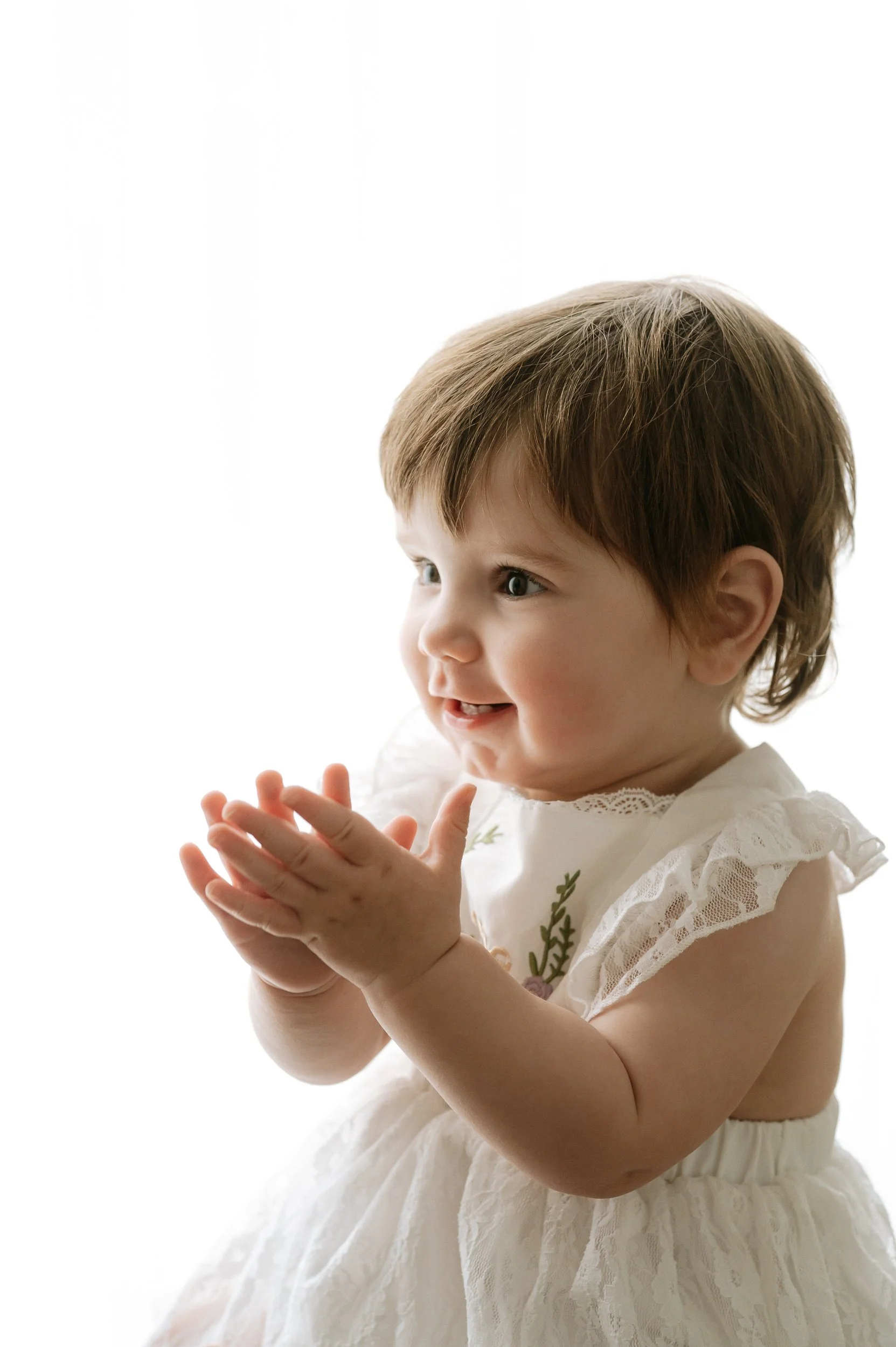 Happy baby girl clapping during a natural light sitter photography session at Alexis Stevenson Photography in Doncaster. Soft, timeless baby portrait in a neutral studio, capturing genuine smiles and milestones for families across South Yorkshire.