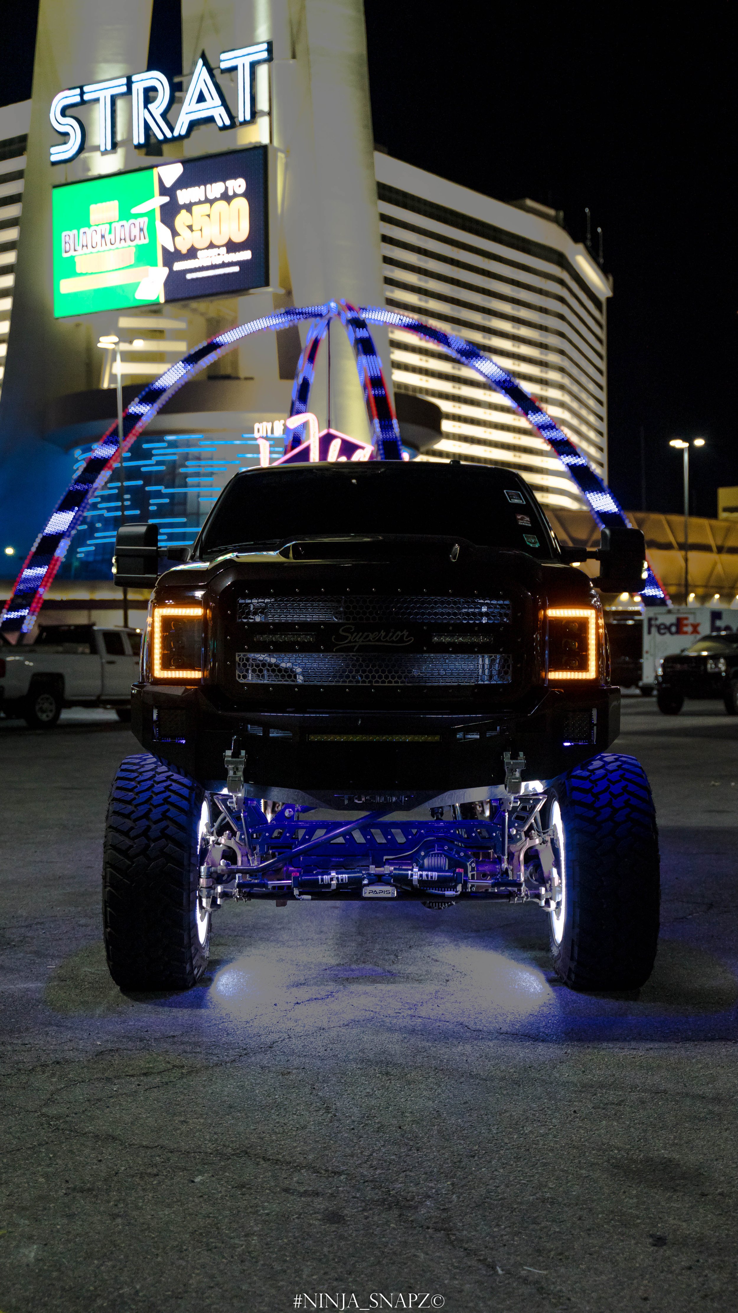 Front view of a our Ford Excursion with illuminated underglow lights parked in front of the Stratosphere Tower at night.