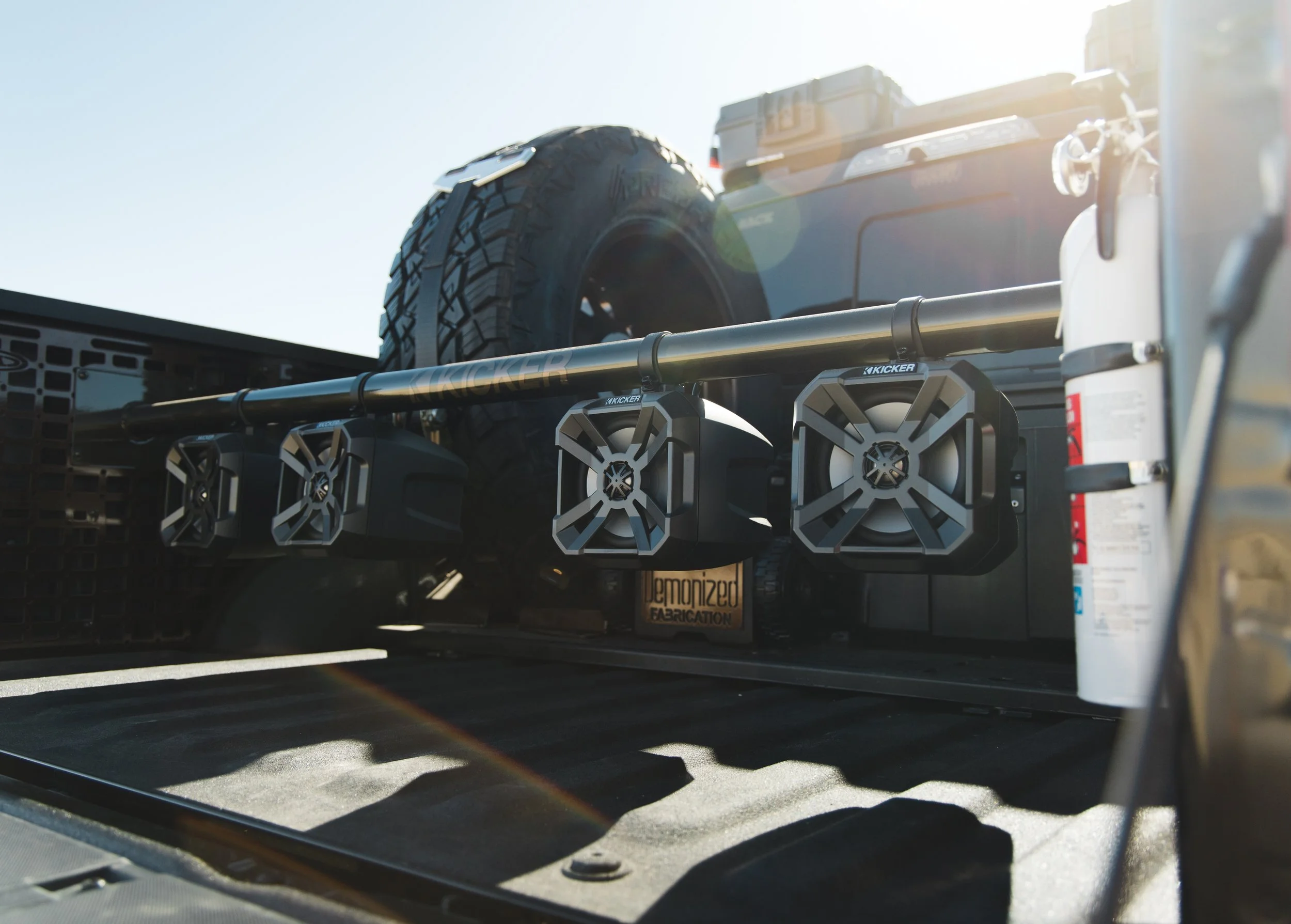 Our Ford F-150 Raptor bed equipped with a mounted spare tire, a cargo box, four speakers mounted on a metal bar in the truck bed.