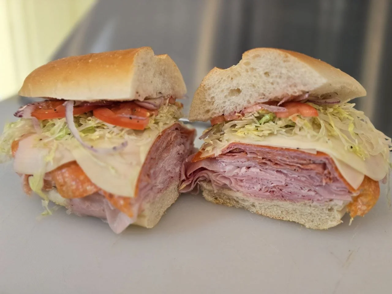 Cut sandwich with layers of ham, turkey, lettuce, tomato, and mayonnaise on a bun.