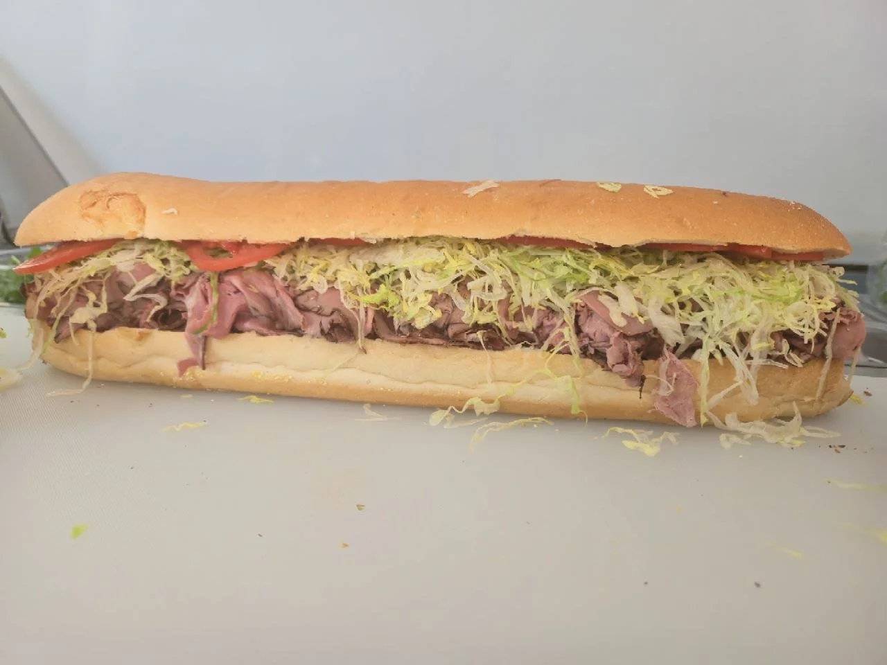 Large submarine sandwich with sliced roast beef, shredded lettuce, sliced tomatoes, and hoagie roll.