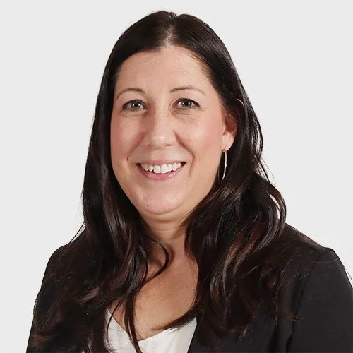 A woman with long, dark brown hair, wearing hoop earrings and a black blazer, smiling against a plain white background.