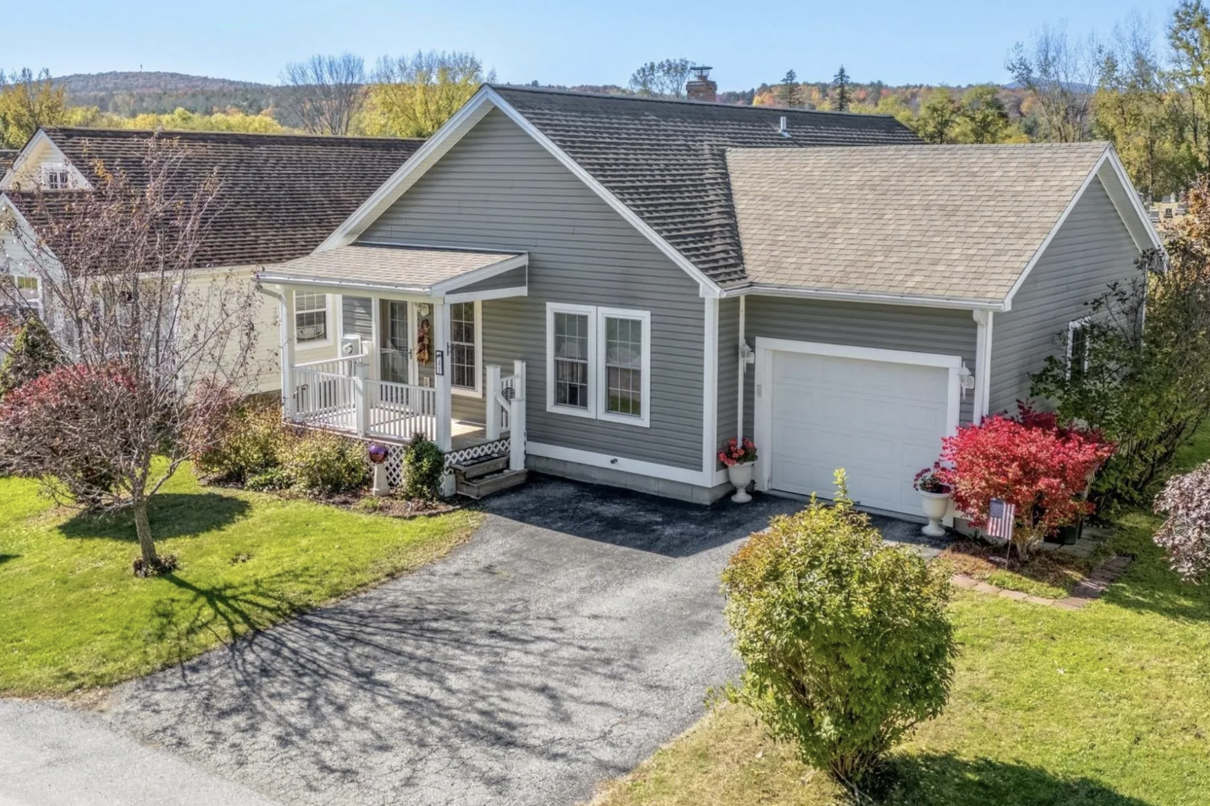 Exterior view of a gray house with a small front porch, a white garage door, and colorful autumn trees in the yard.