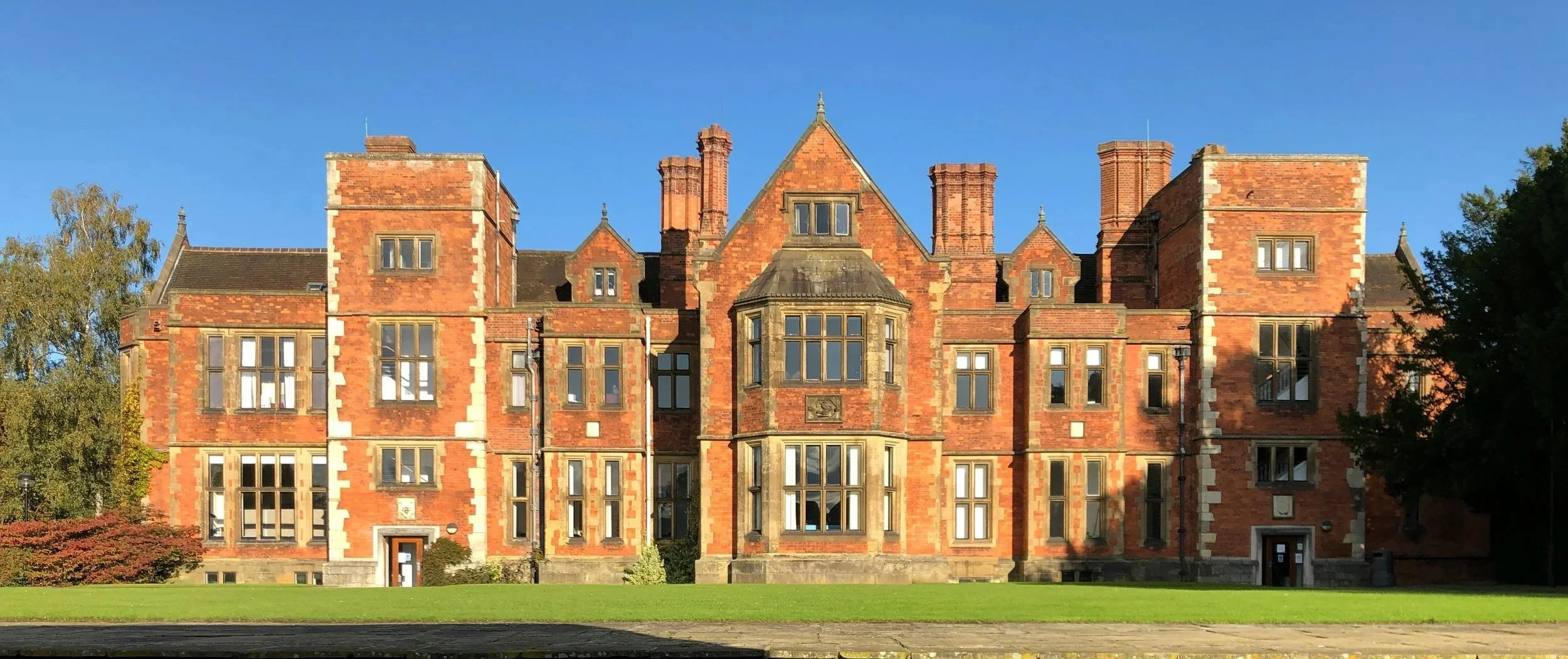 A large historic red brick building with multiple windows, towers, and chimneys, set against a clear blue sky.