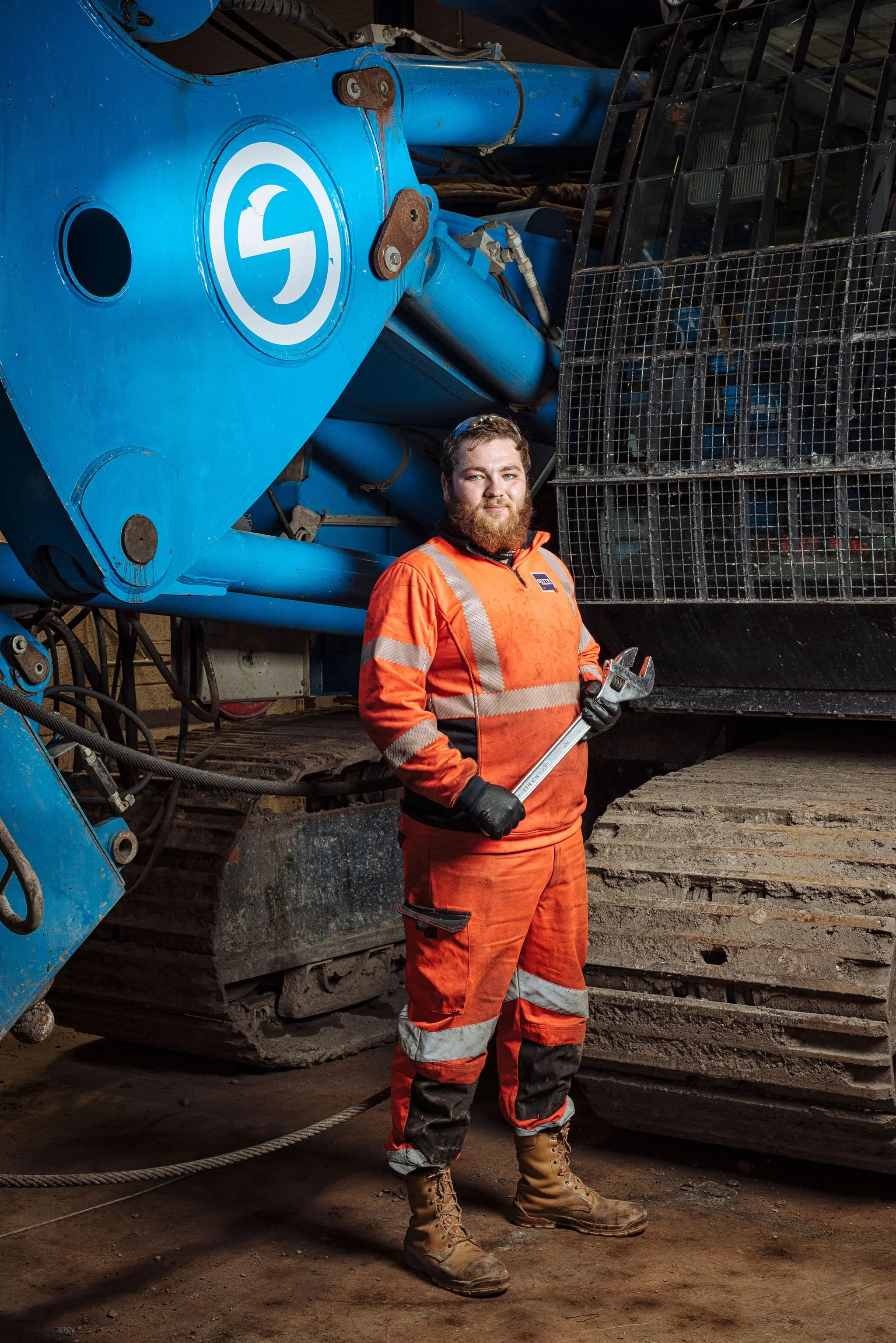 Photographe portrait, mécanicien avec outil devant un engin de chantier.