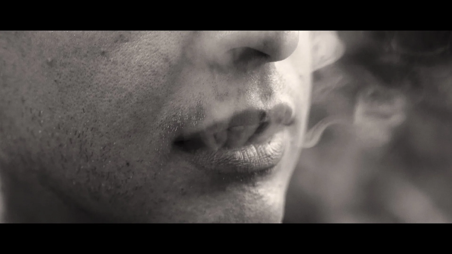 Close-up of a person's face in black and white, focusing on lips and nose, with smoke near their mouth.