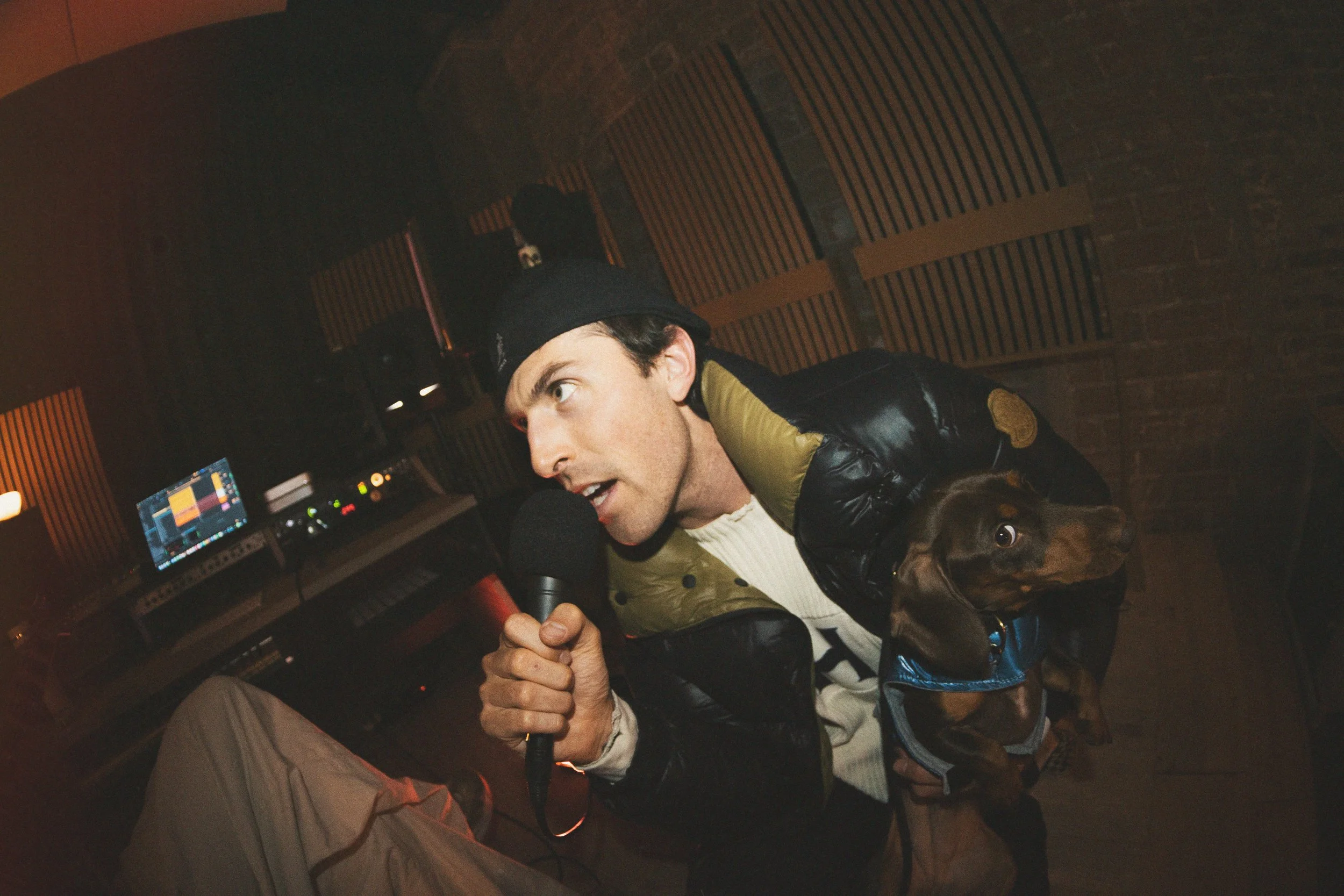 A man singing into a microphone in a recording studio with a dog on his lap.