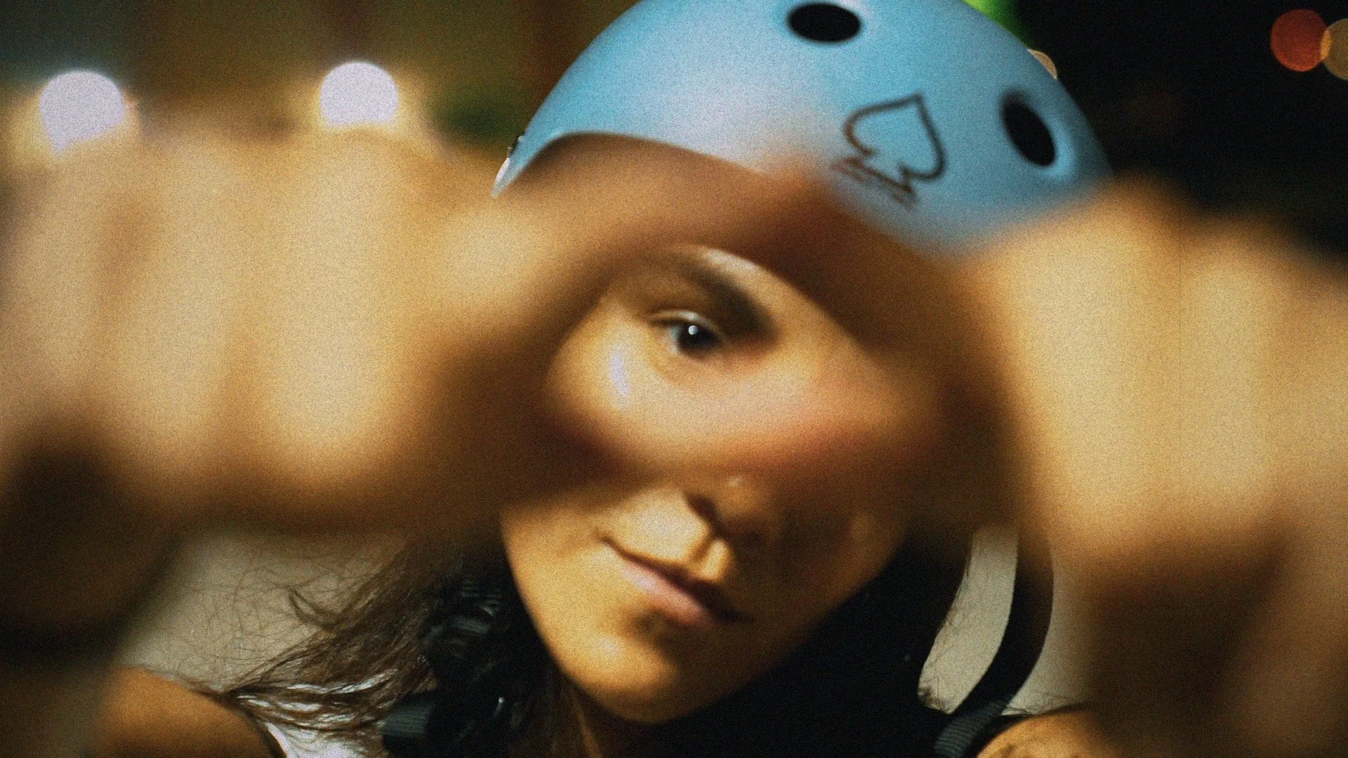 A woman wears a bike helmet with a blue and white design. She is looking directly at the camera with her face framed by a blurred foreground.