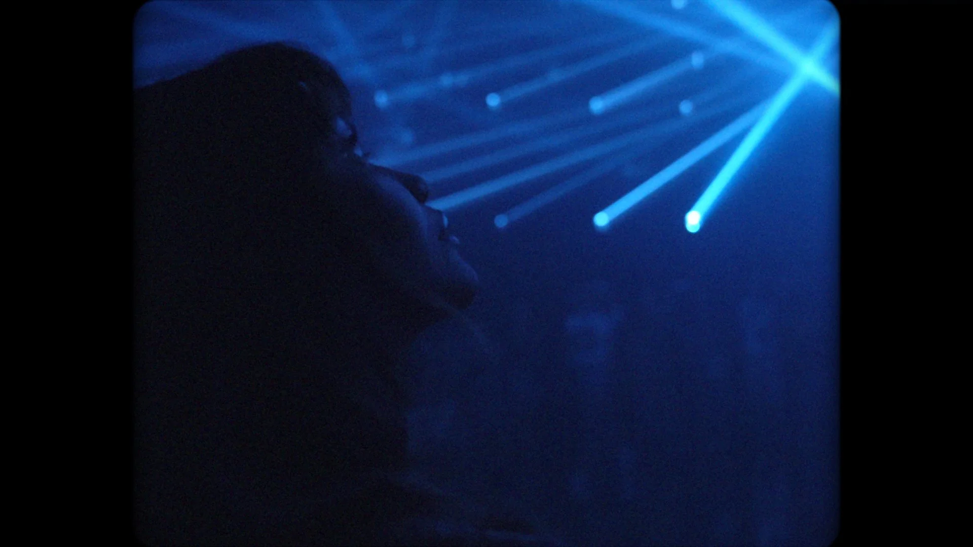 A person in profile watching blue laser lights in a dark room.