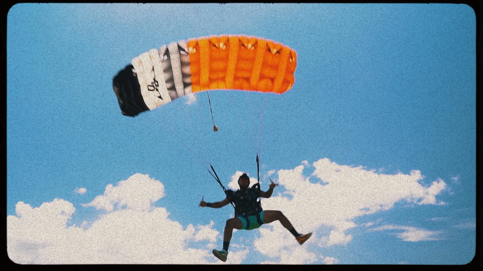 Person paragliding in a clear sky with a colorful parachute, smiling and waving.