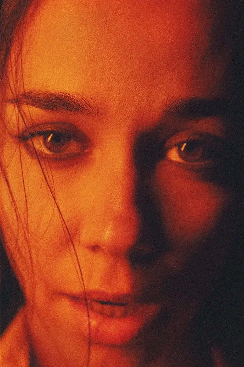 Close-up of a woman's face with a warm, orange-toned lighting, showing her eyes, eyebrows, and partially visible lips.