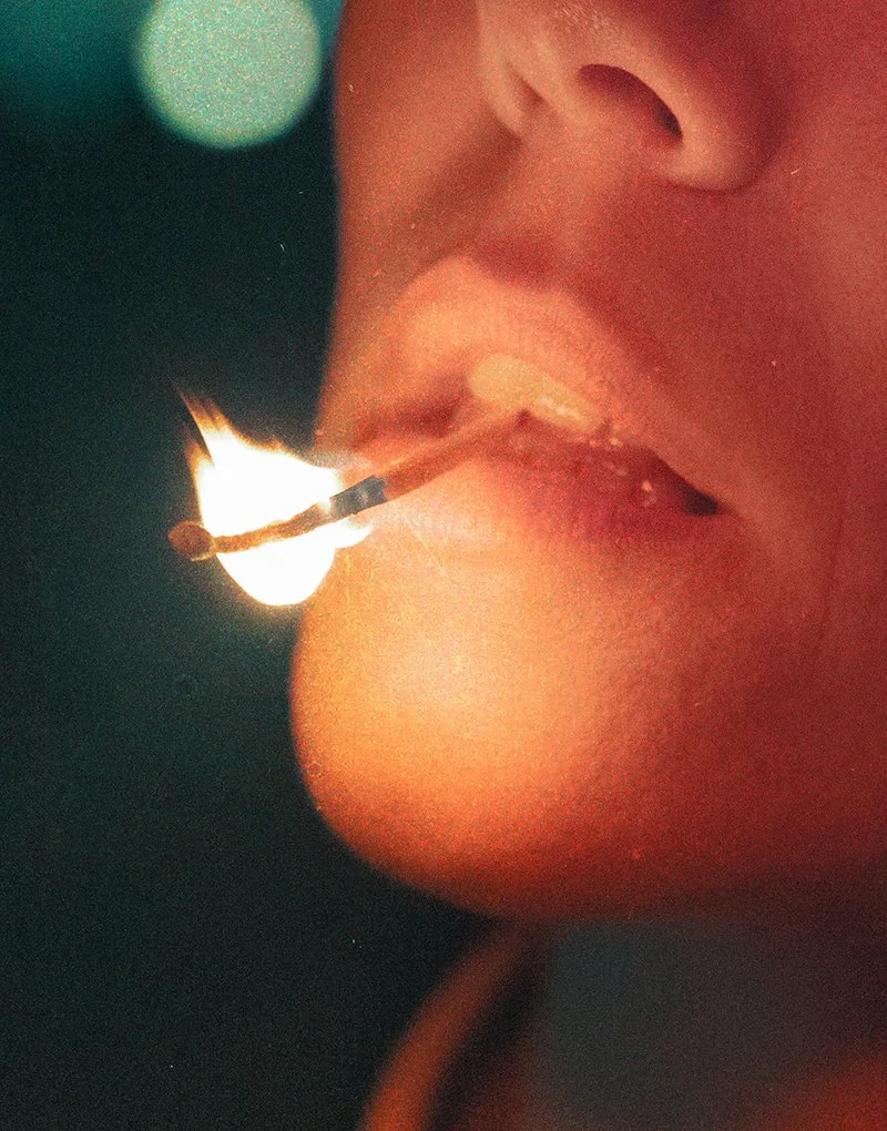 Someone lighting a match near their lips in a close-up shot.