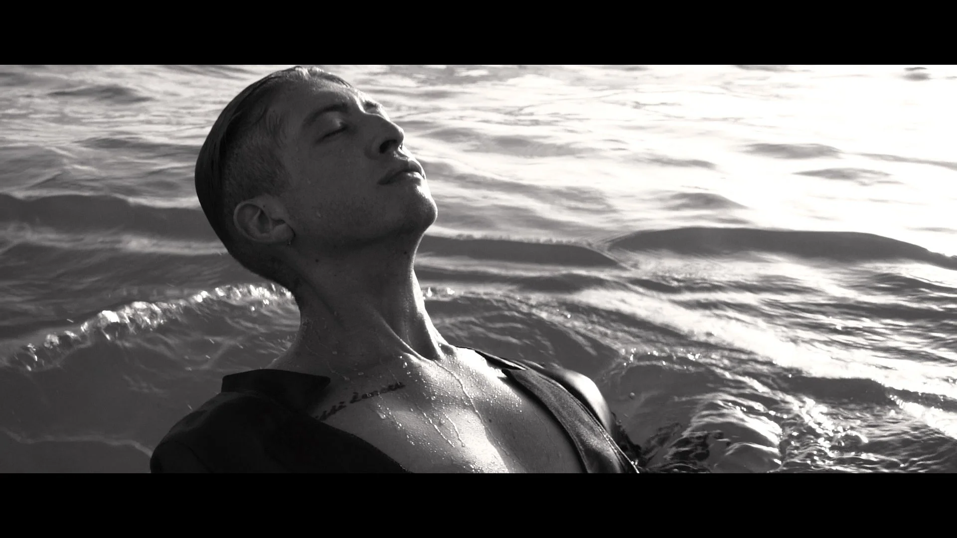 Black and white photo of a person with wet hair submerged in water with their eyes closed and head tilted back.