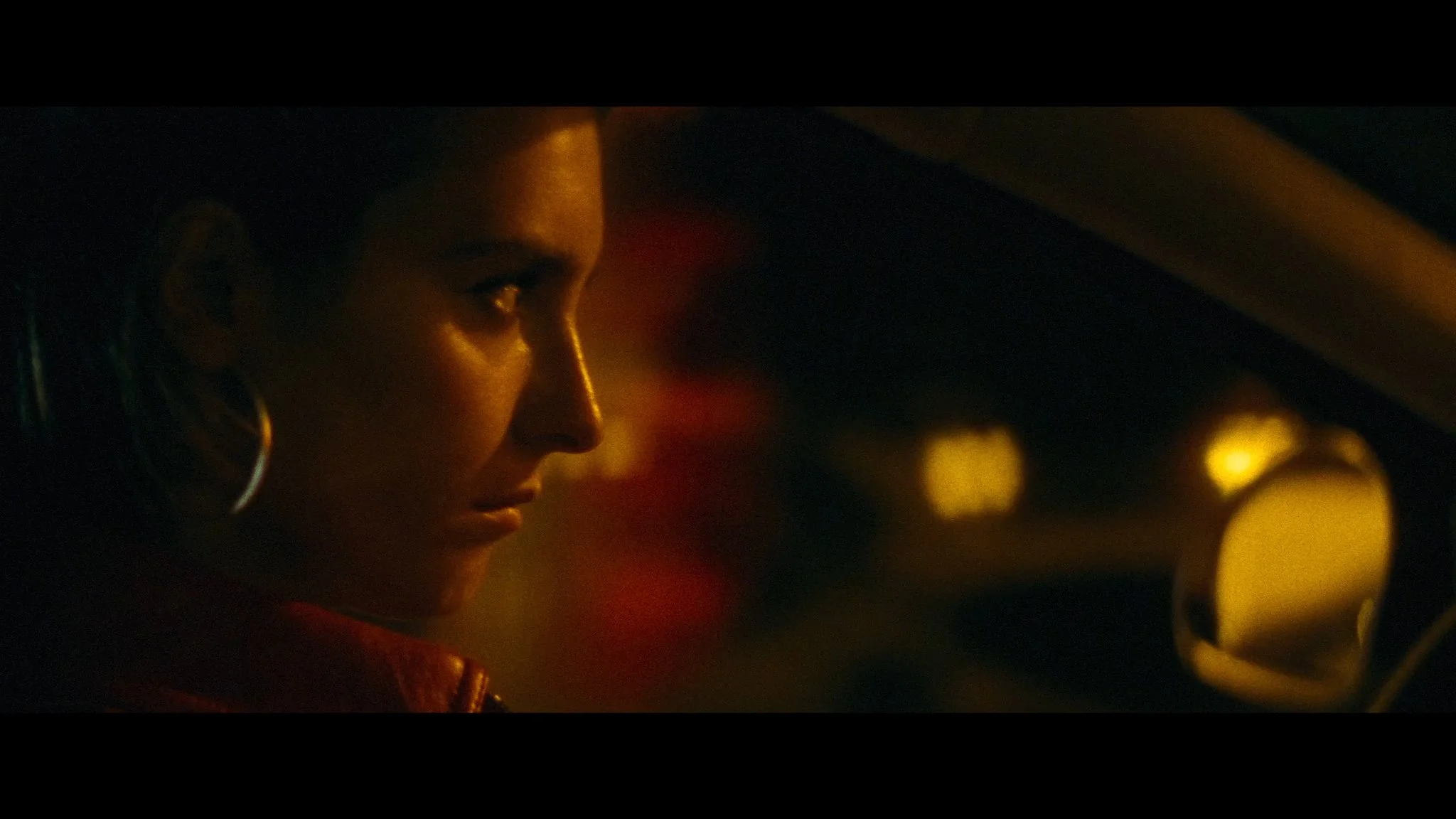 Close-up of a woman with earrings inside a car at night, with warm dim lighting