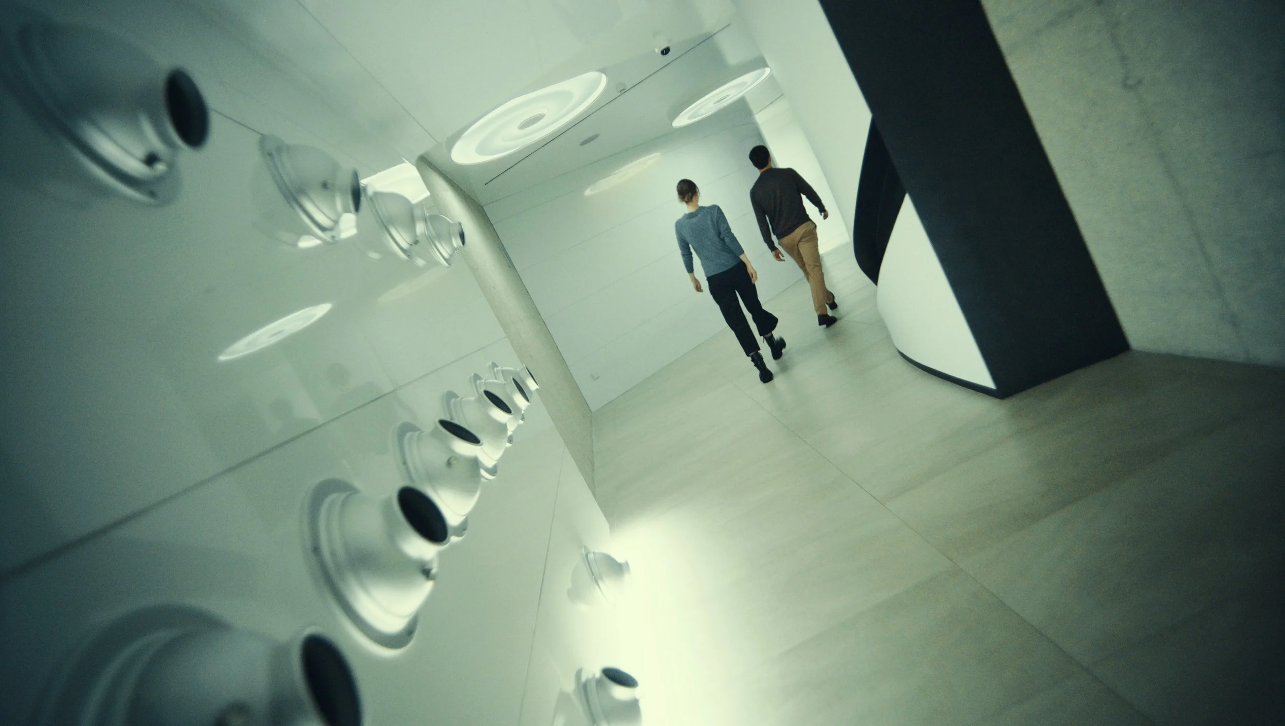 Two people walking side by side down a bright, modern corridor with white walls and a curved corner.